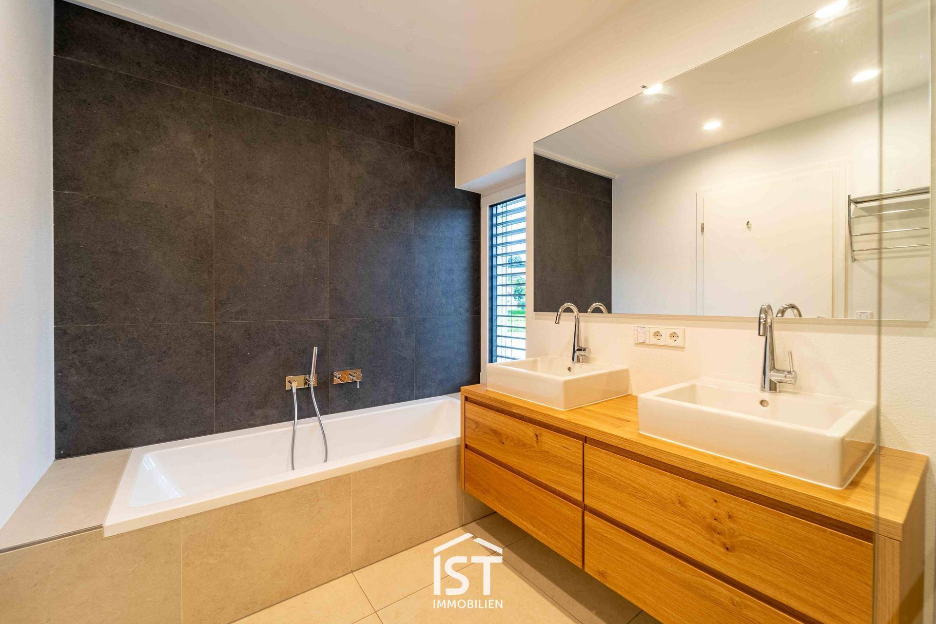 Modernes Badezimmer mit Doppelwaschbecken, Badewanne und dunklen Wandfliesen.