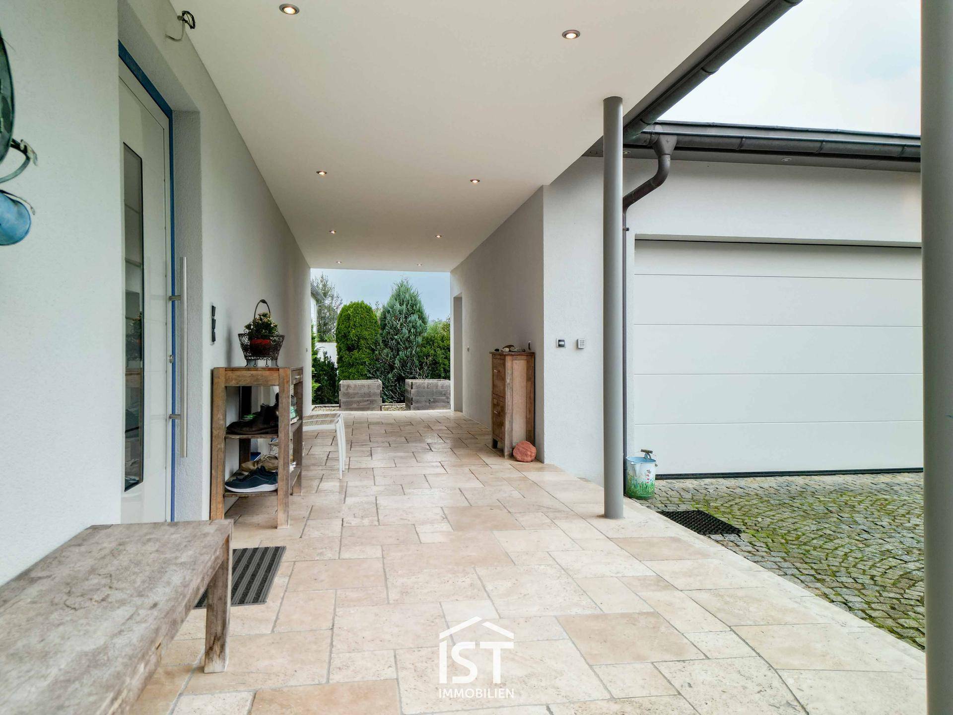 Überdachter Eingangsbereich und Carport mit Garagenzugang und Steinplattenboden.