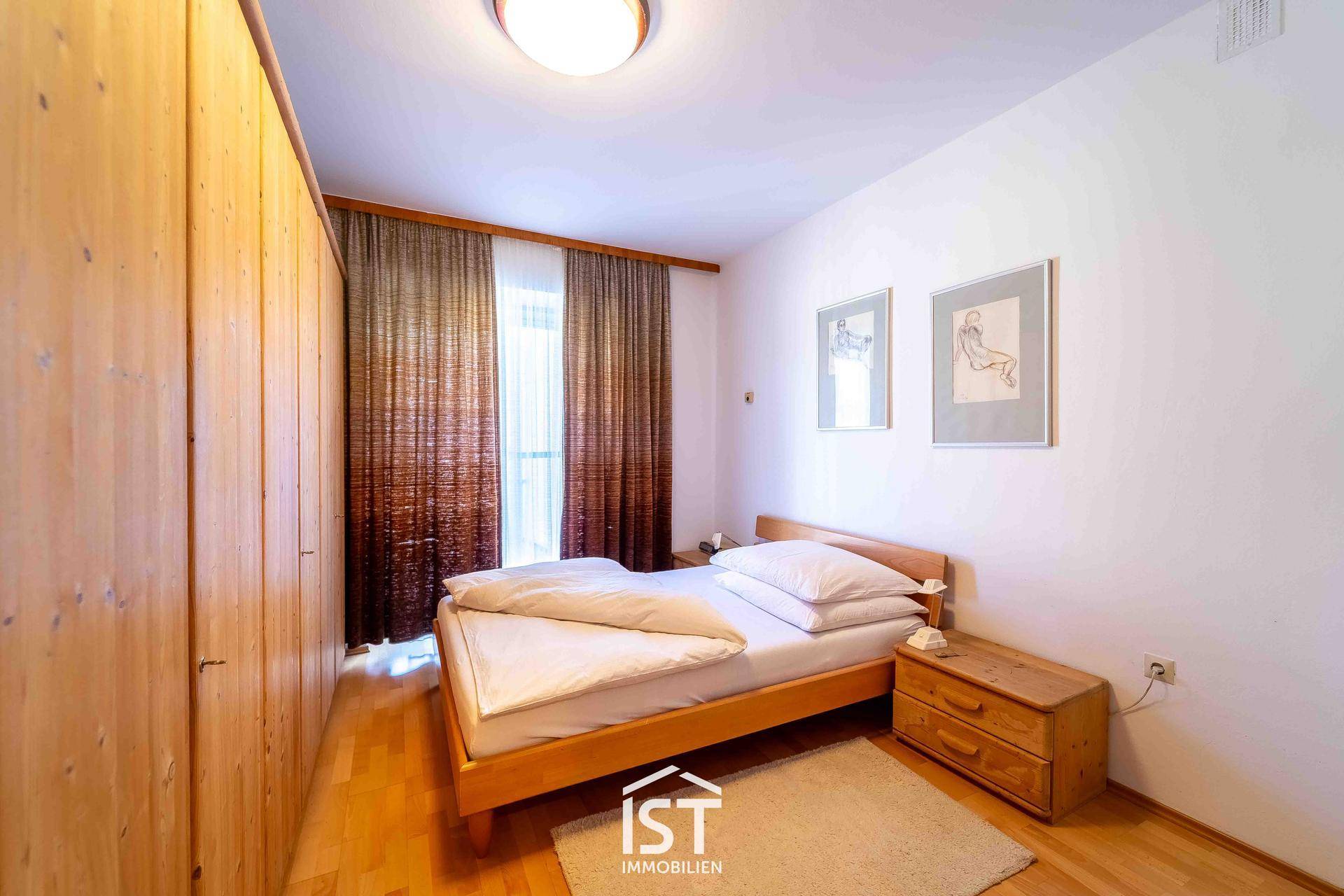 Schlafzimmer mit Holzbett, Kleiderschrank und Parkettboden, hell und gemütlich.