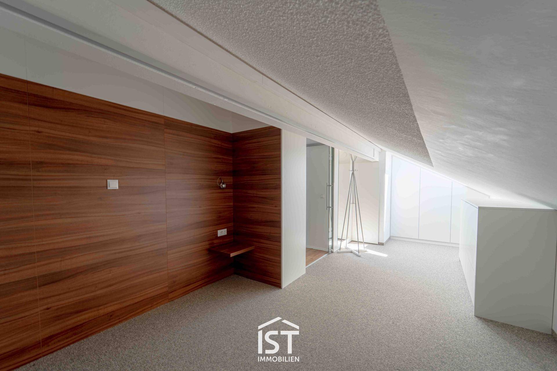 Schlafzimmer mit Holzwandverkleidung, Teppichboden und schrägen Decken im Dachgeschoss.