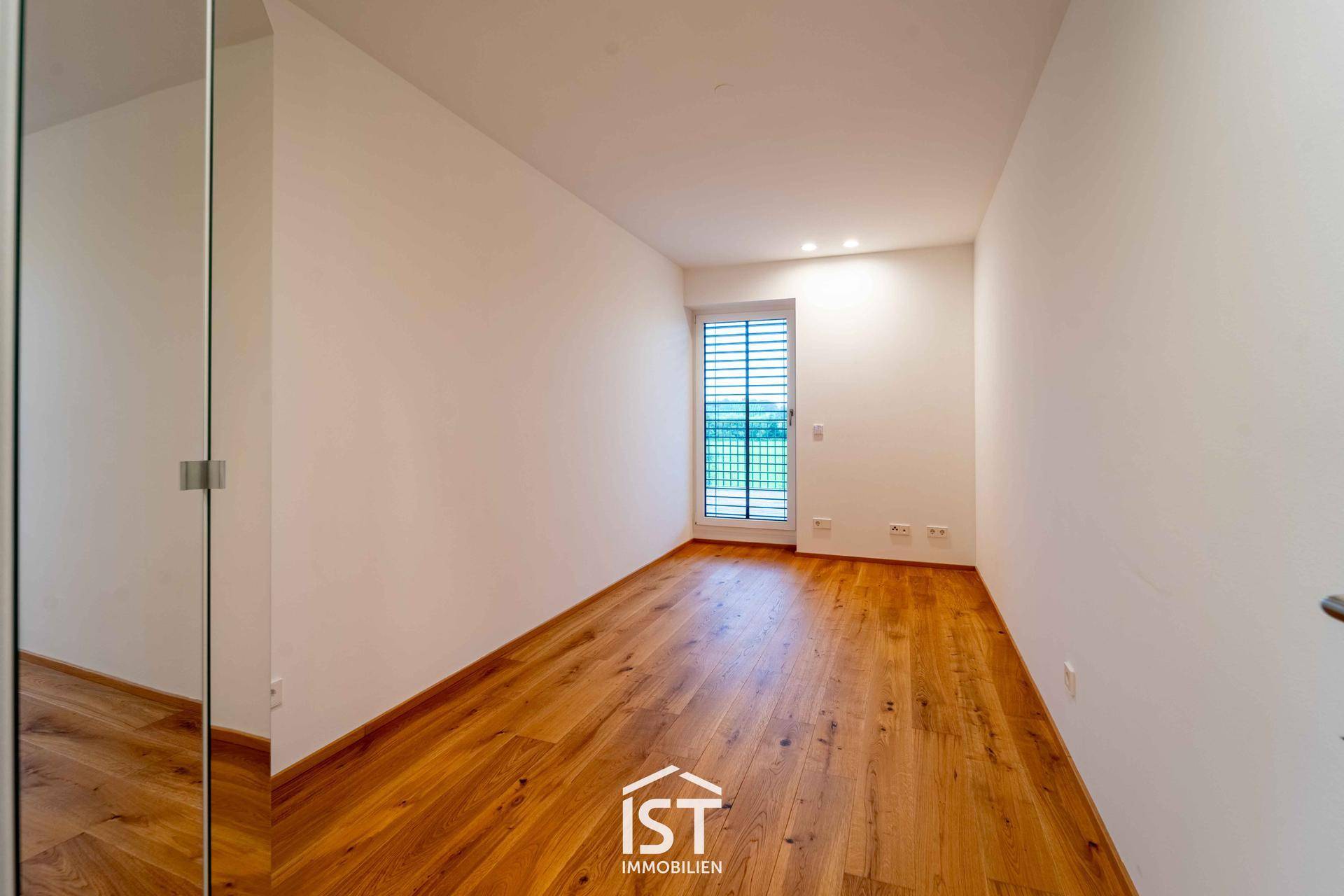Schlafzimmer mit Holzboden und Zugang zu einem Balkon, bietet viel Tageslicht.