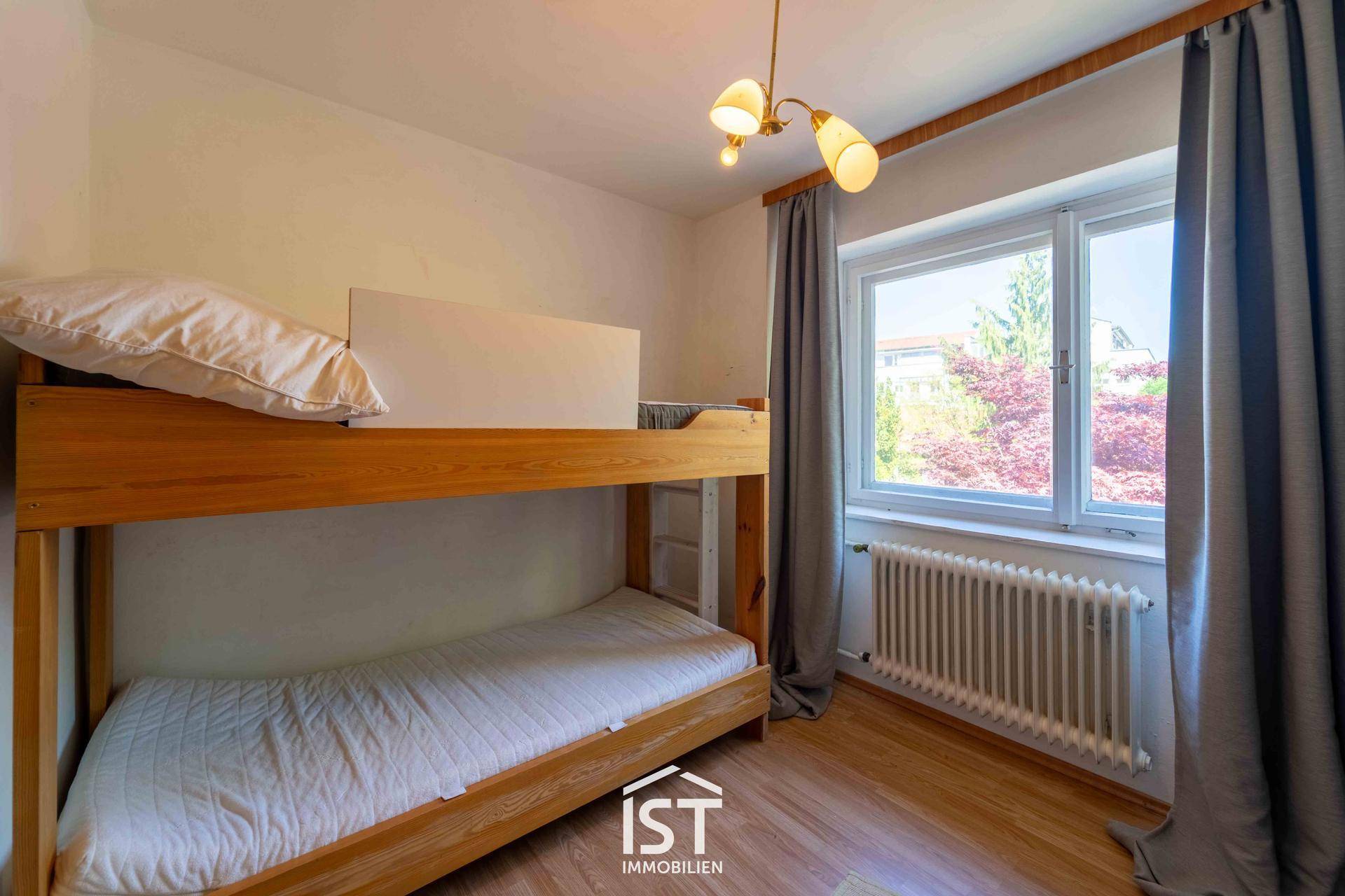 Kinderzimmer mit Etagenbett und Fenster, das viel Tageslicht hereinlässt.