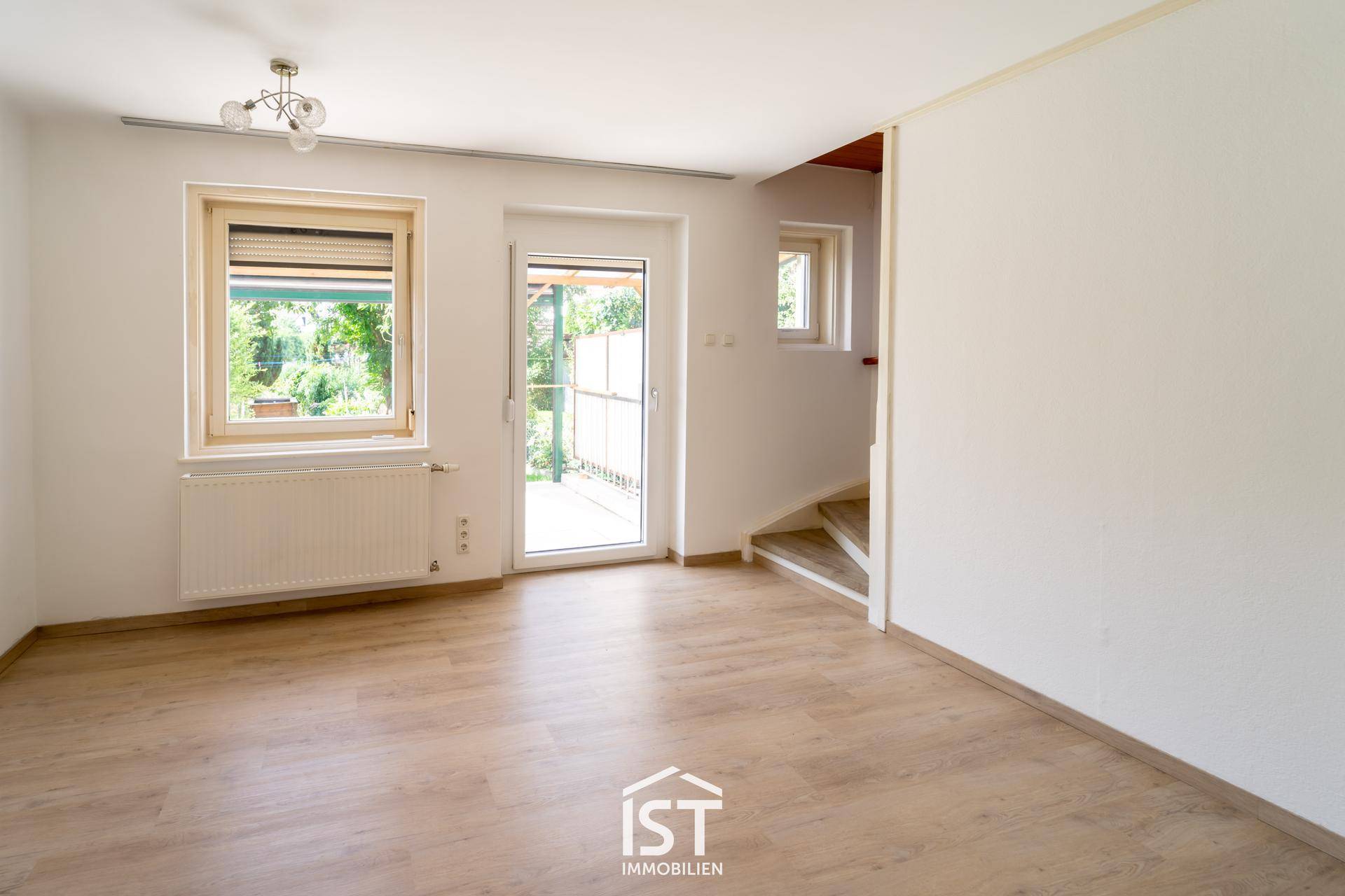 Geräumiges Wohnzimmer mit Laminatboden, großen Fenstern und direktem Zugang zur Terrasse.
