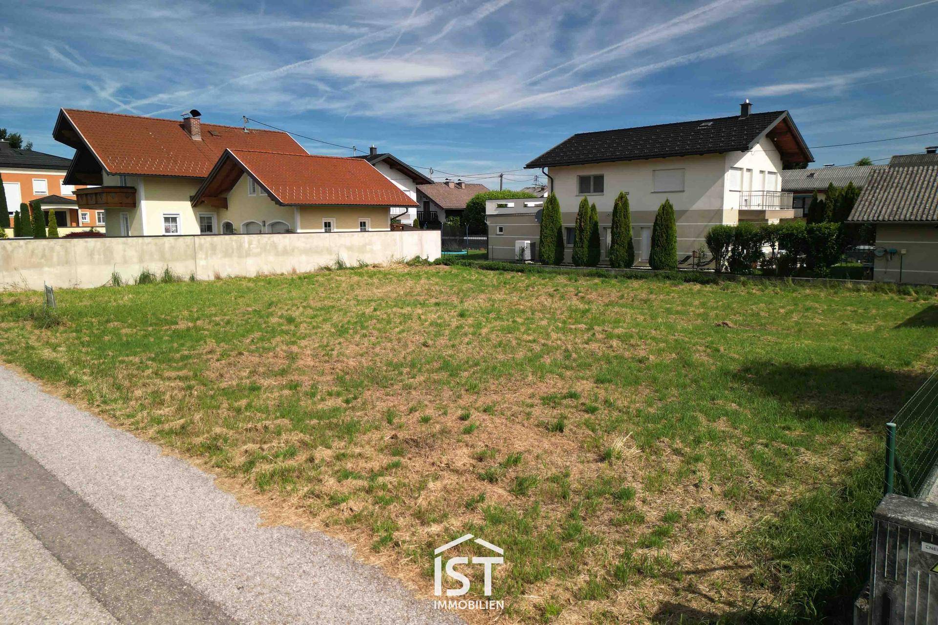Blick über das sonnige, unbebaute Grundstück mit umliegenden Wohnhäusern und grüner Umgebung.