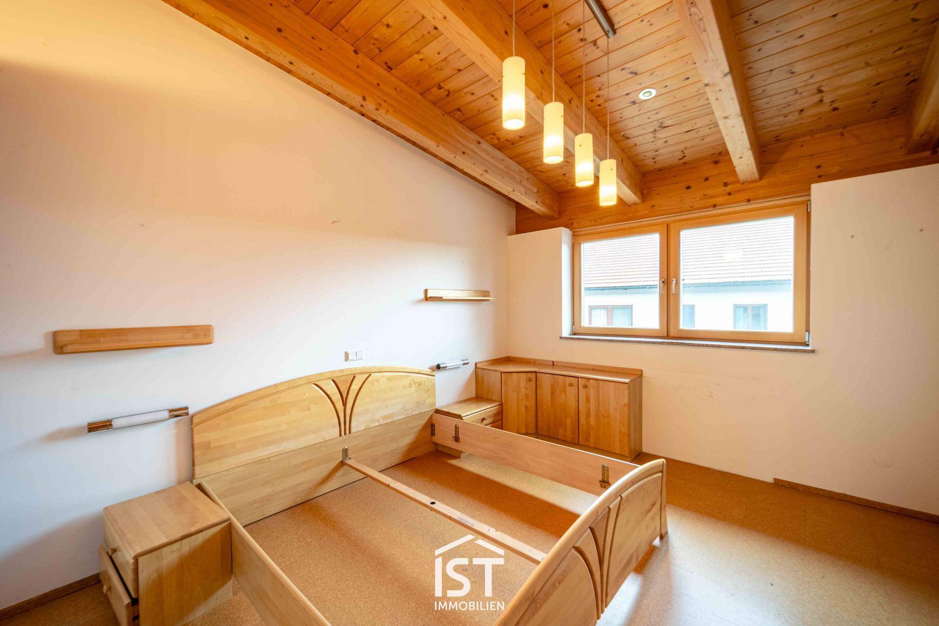 Helles Schlafzimmer mit Holzbalkendecke, Holzbett und Blick ins Grüne.