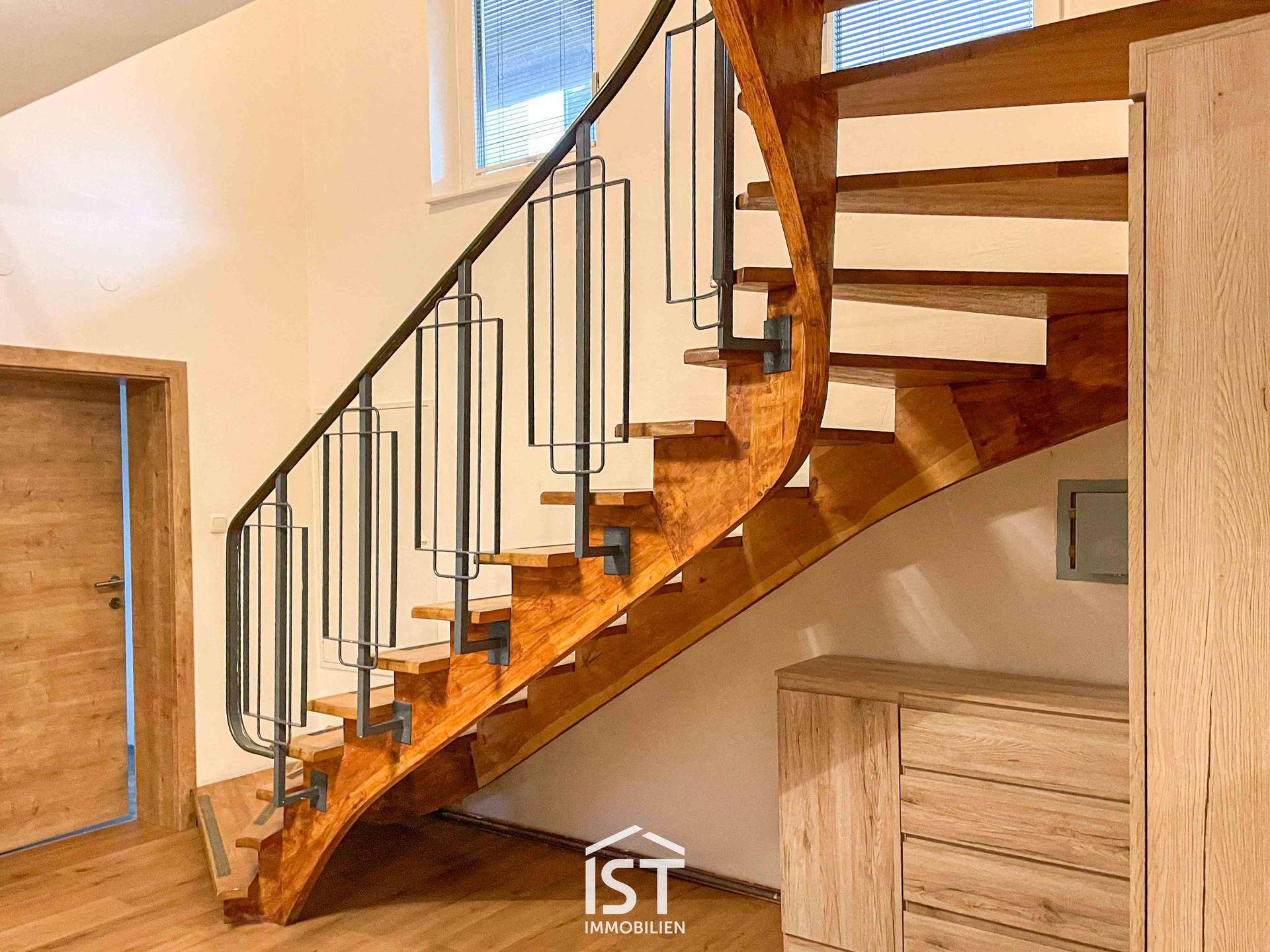 Elegante Holztreppe mit schmiedeeisernem Geländer in einem hellen Eingangsbereich mit Holzfußboden.