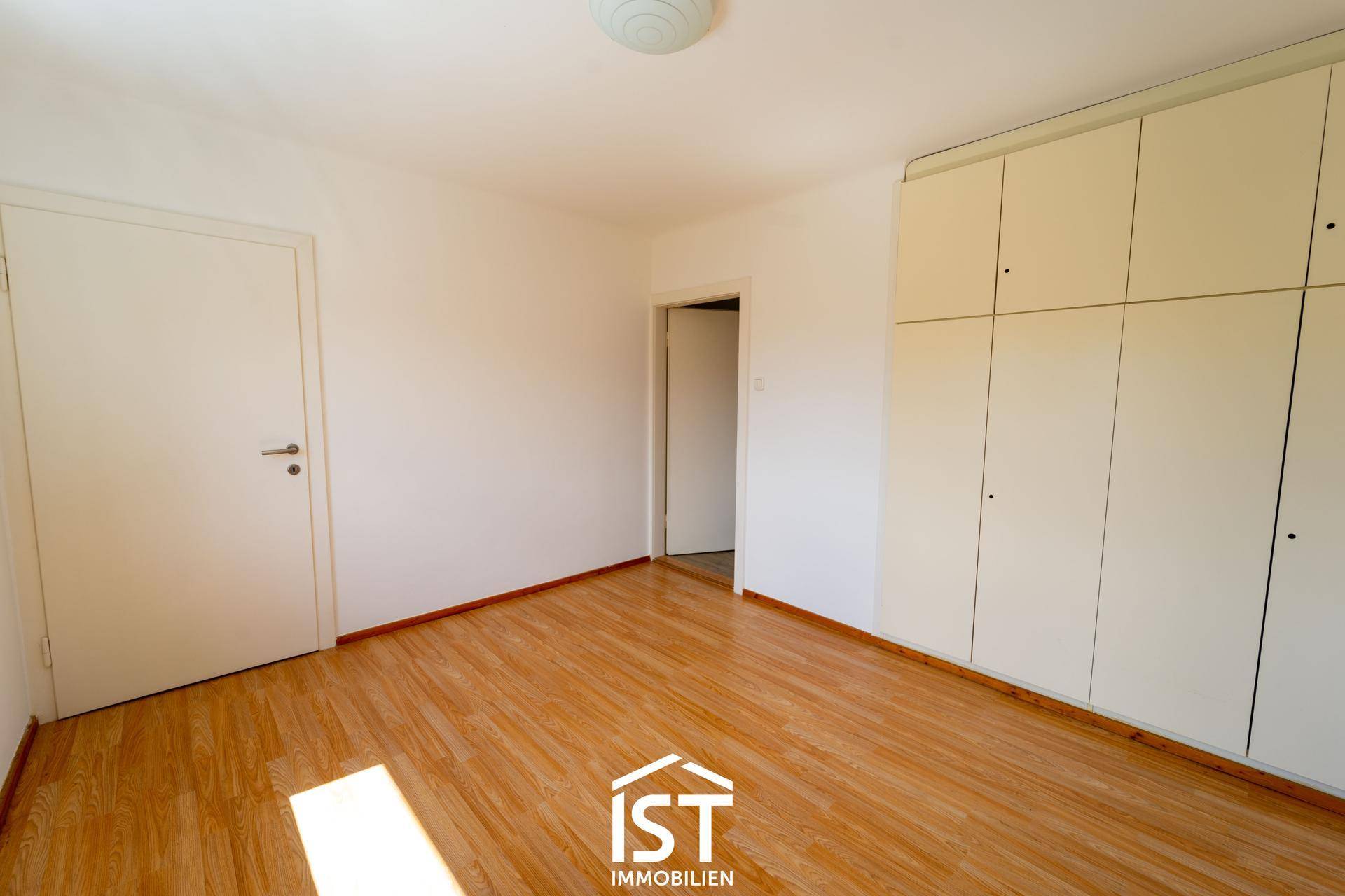 Schlafzimmer mit Laminatboden und praktischen Einbauschränken entlang einer Wand.