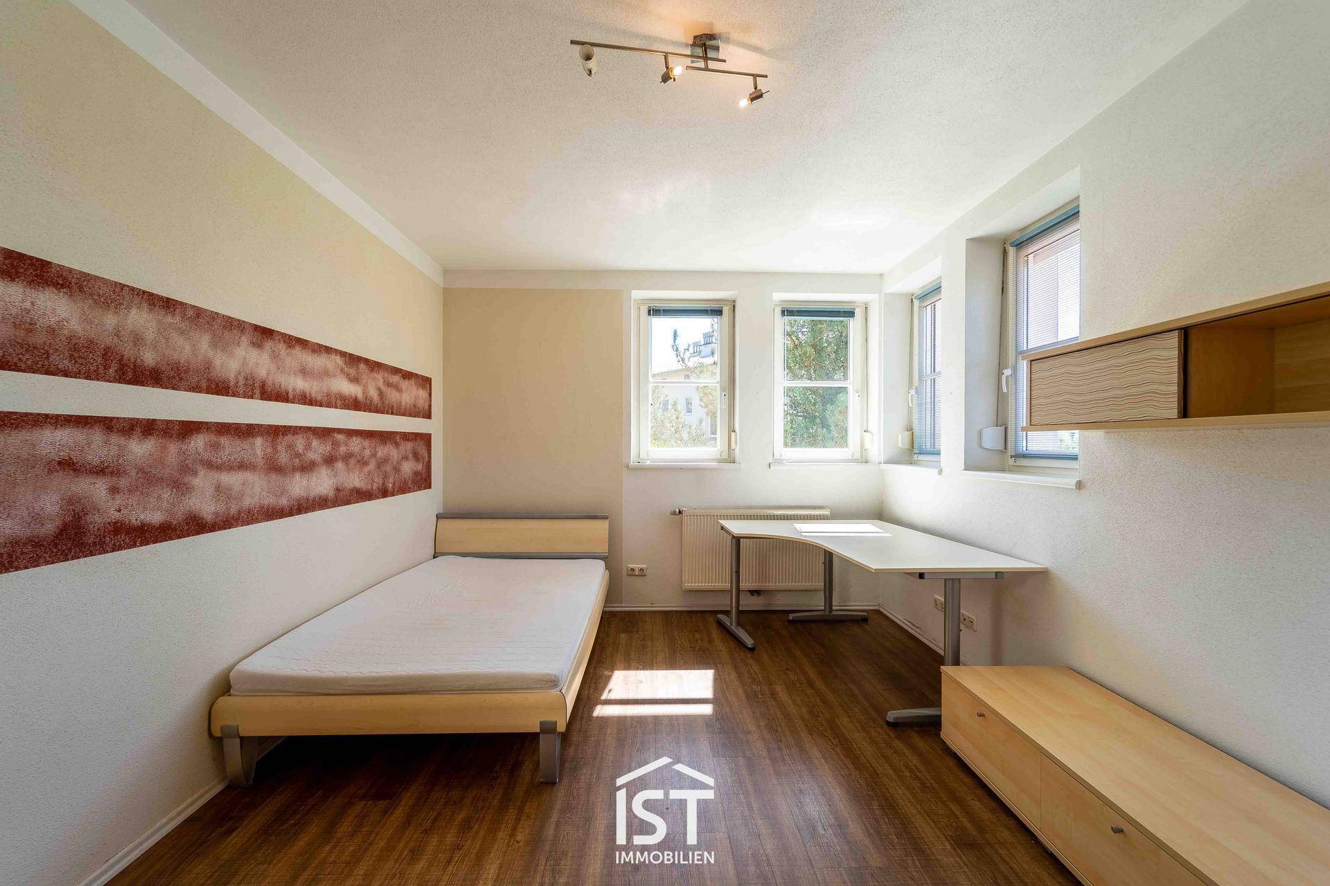 Helles Schlafzimmer mit Einzelbett, Schreibtisch und Laminatboden.