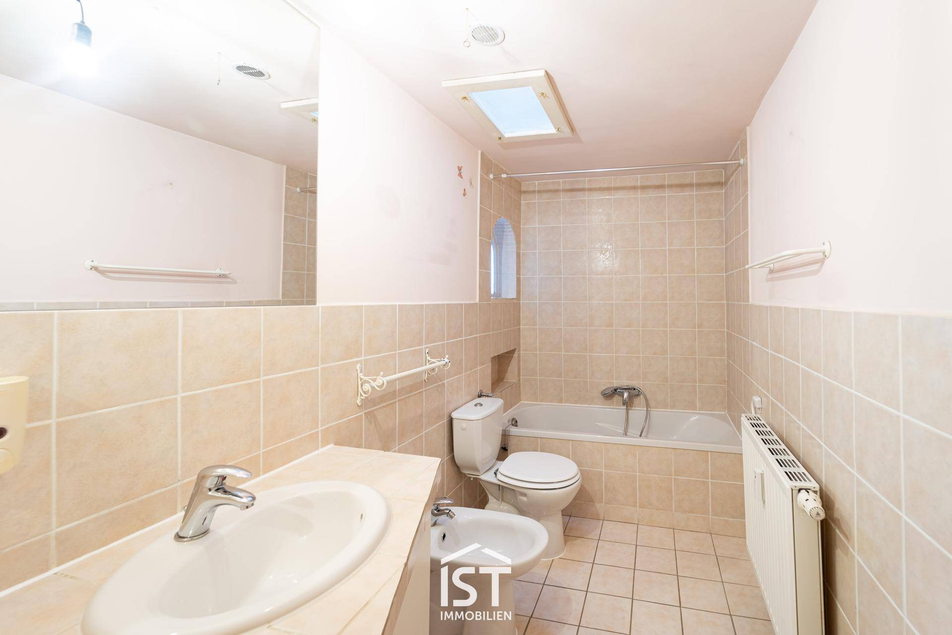 Badezimmer mit Badewanne, Bidet und beigefarbenen Fliesen.