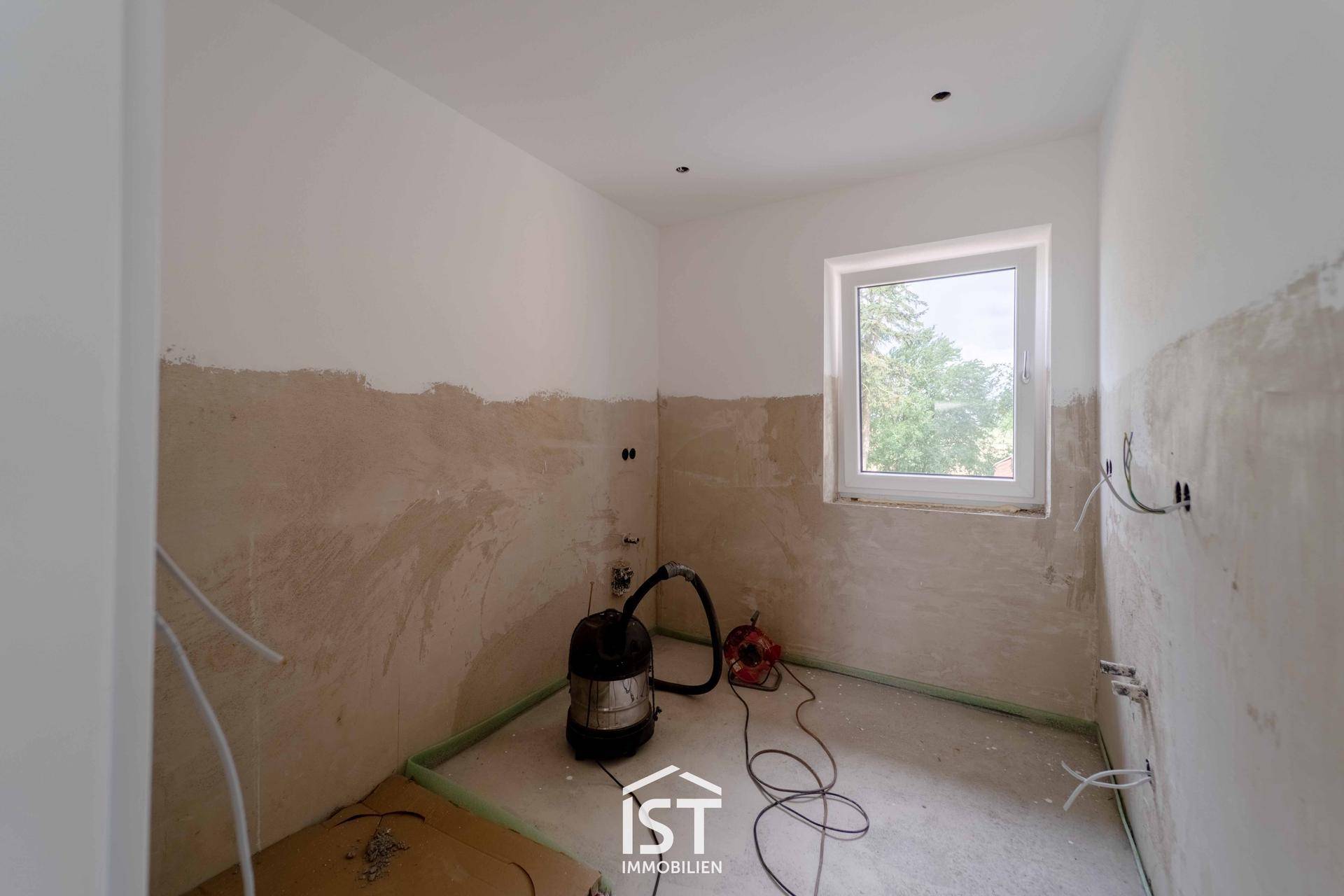 Unfertiges Badezimmer oder Hauswirtschaftsraum mit Fenster und vorbereiteten Sanitäranschlüssen.