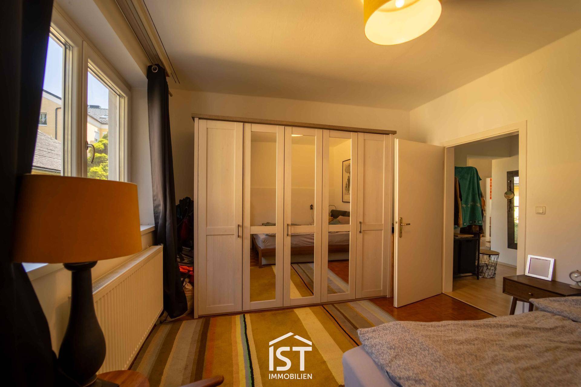 Schlafzimmer mit großem Spiegelschrank, gemütlichem Bett und Fenster mit Blick nach draußen.