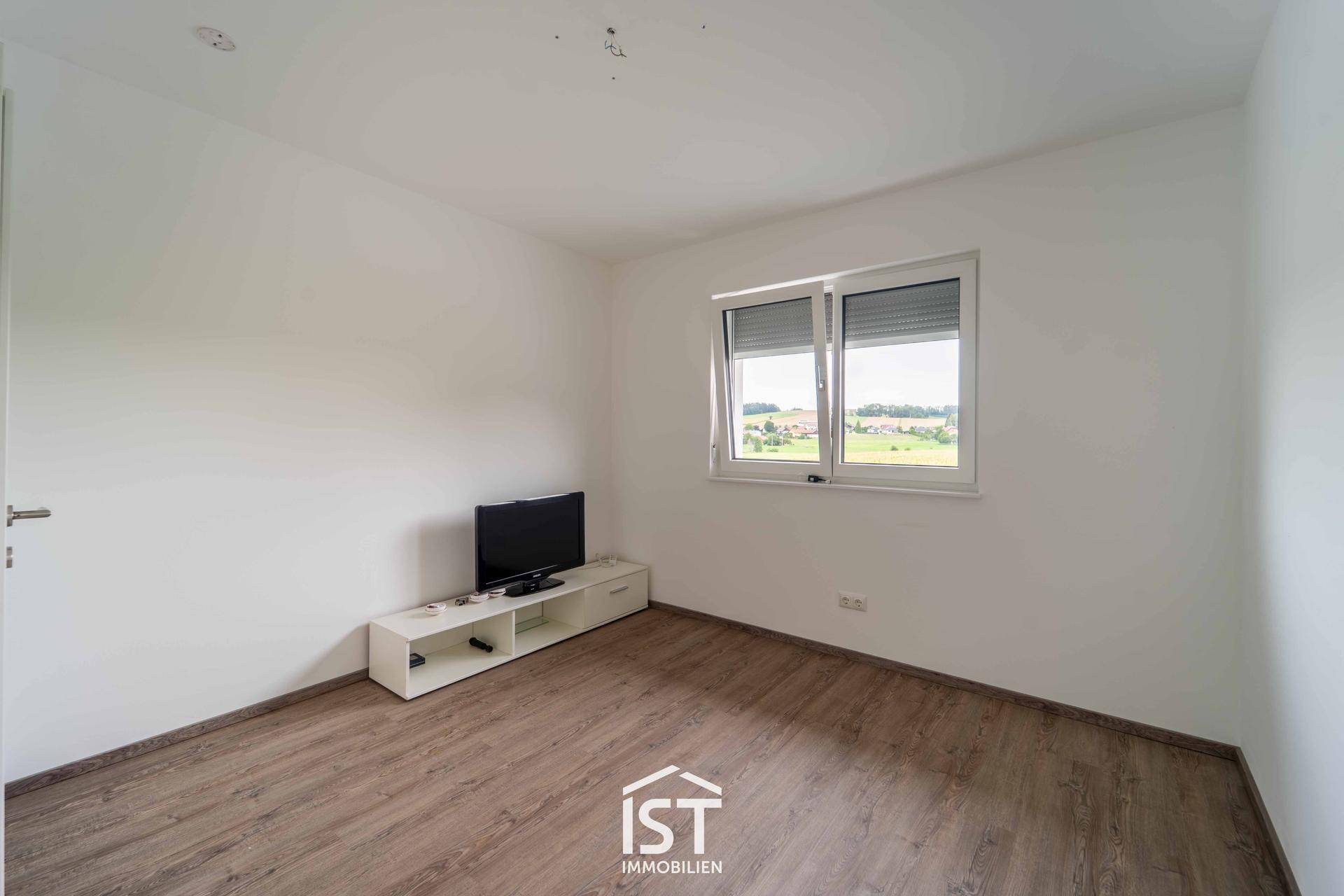 Gemütliches Schlafzimmer mit Laminatboden, Fenster und Blick ins Grüne.