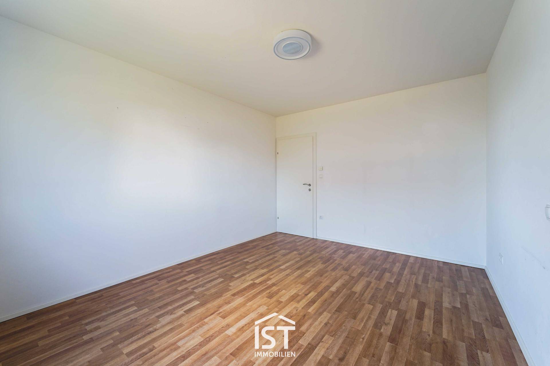 Leeres Zimmer mit Holzboden und weißen Wänden, bereit zur individuellen Gestaltung.