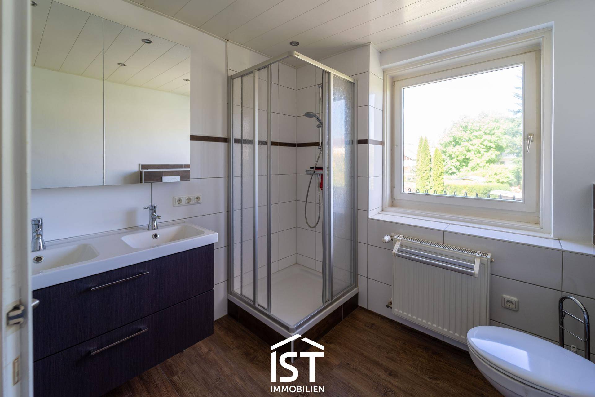 Modernes Badezimmer mit Doppelwaschbecken, Duschkabine und Fenster mit Blick ins Grüne.