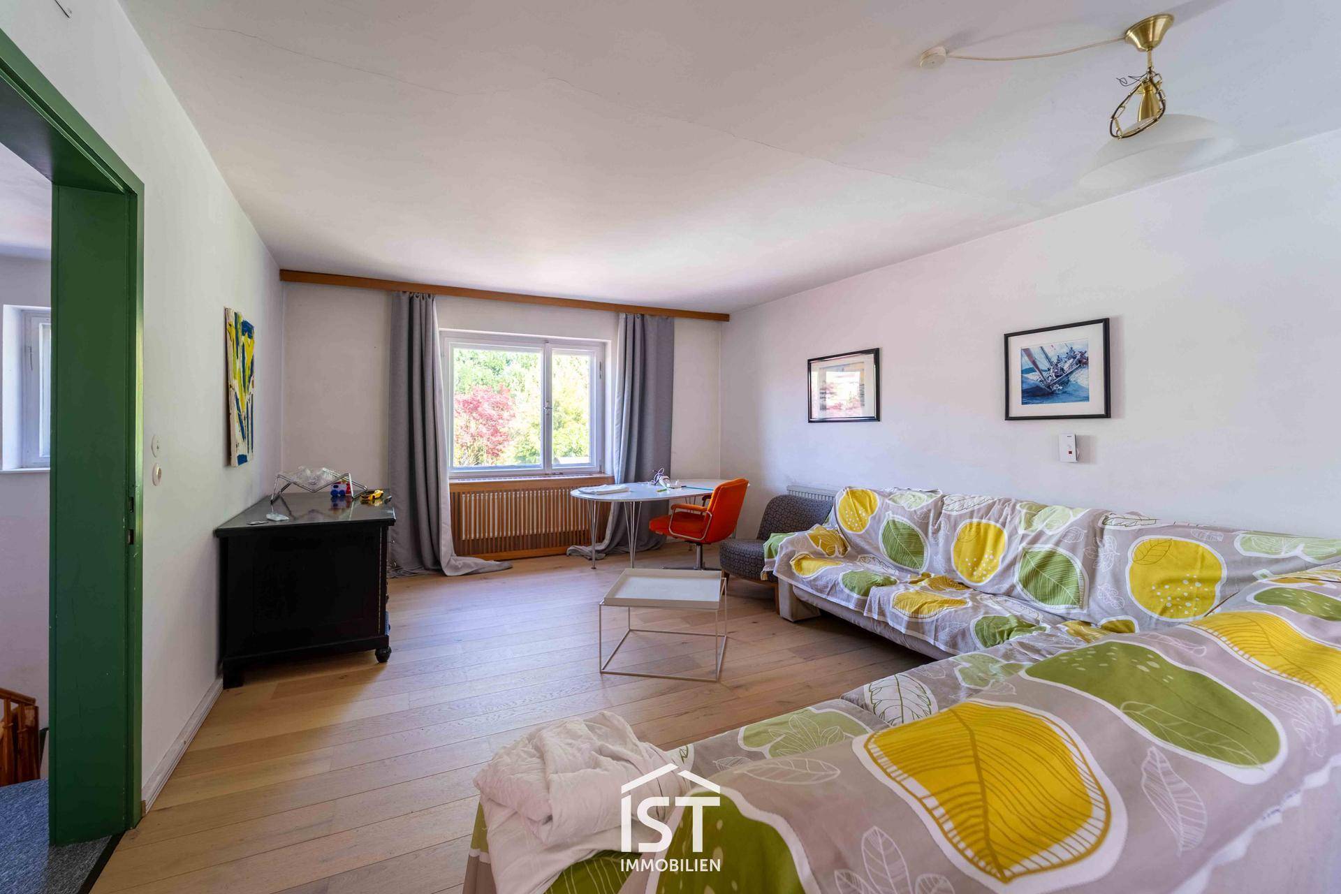 Helles Wohnzimmer mit Sofa, kleinem Tisch und Blick ins Grüne durch das Fenster.