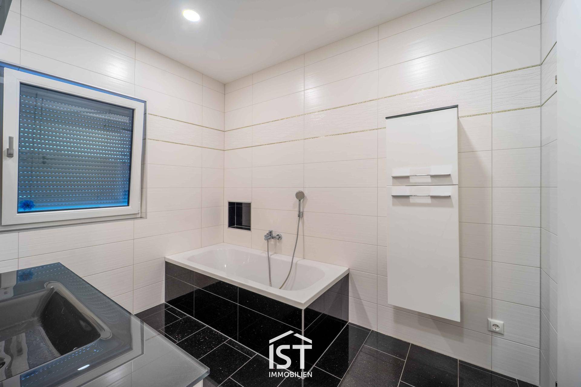Modernes Badezimmer mit Badewanne, Fliesen in Schwarz-Weiß und Fenster.