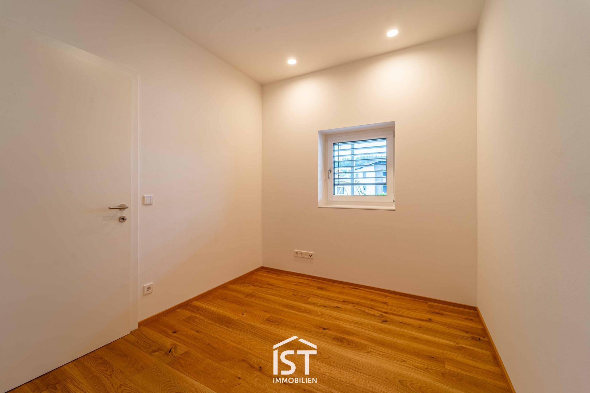 Helles Zimmer mit Holzparkett und einem Fenster, ideal als Schlaf- oder Arbeitszimmer.