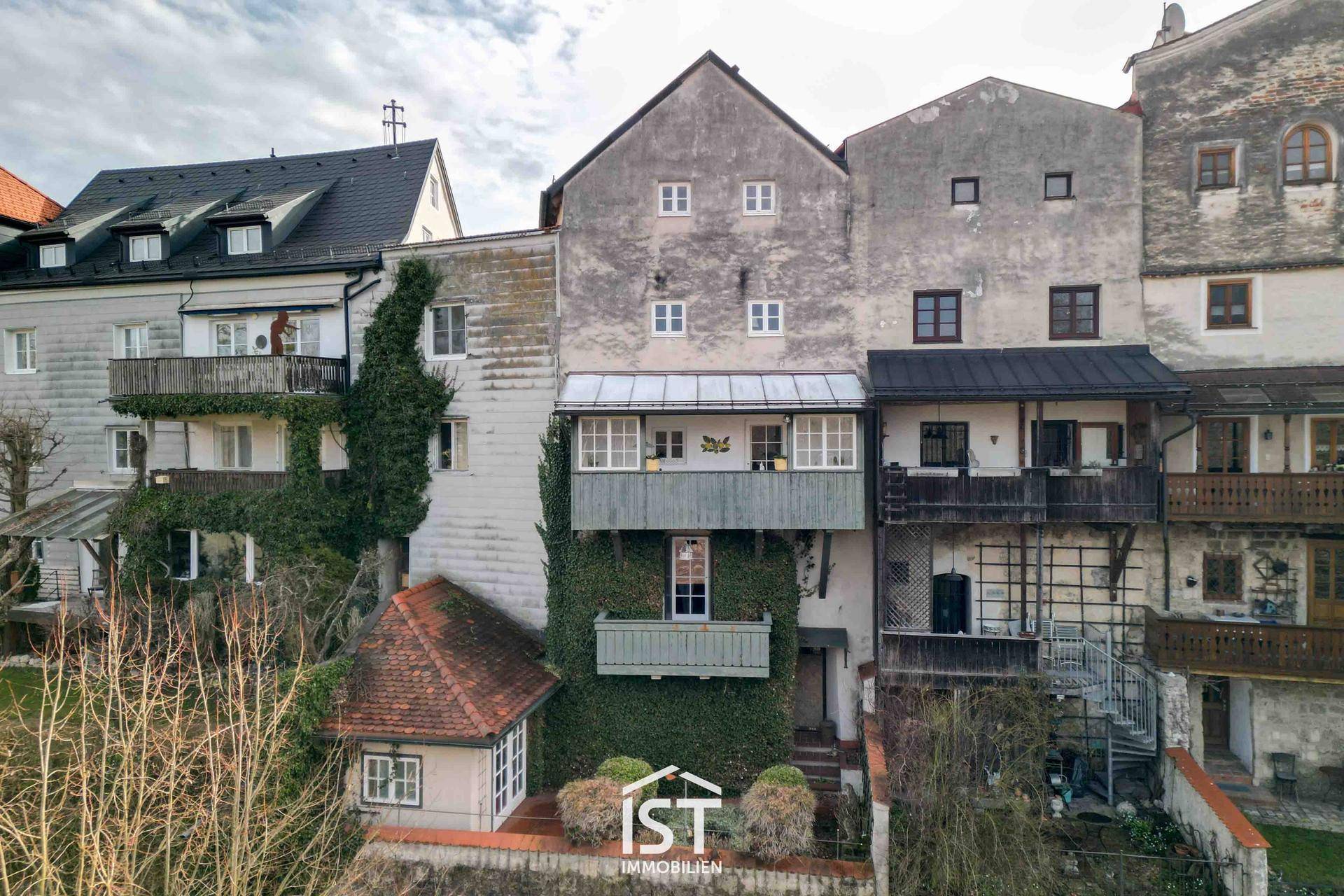 Rückansicht historischer Gebäude mit begrünten Fassaden und mehreren Balkonen über einem Hang.