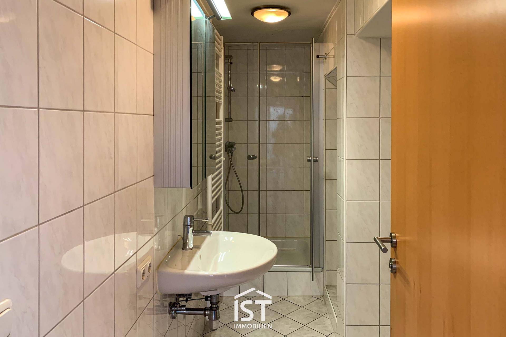 Gefliestes Badezimmer mit Dusche, Waschbecken und Spiegelschrank.