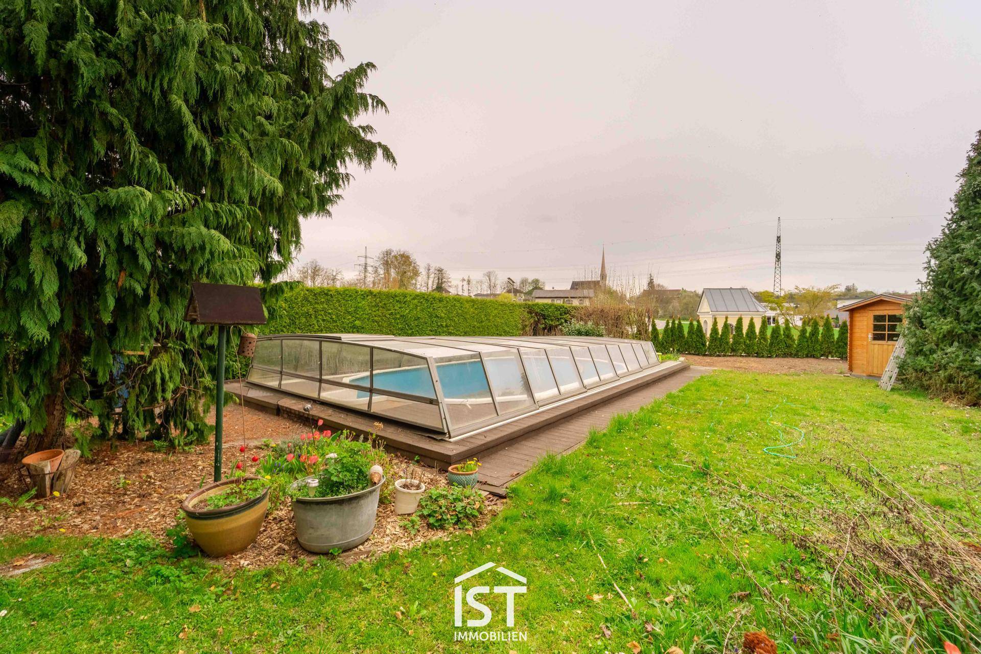 Großer Garten mit überdachtem Pool, Rasenfläche und hohen Hecken für Privatsphäre.