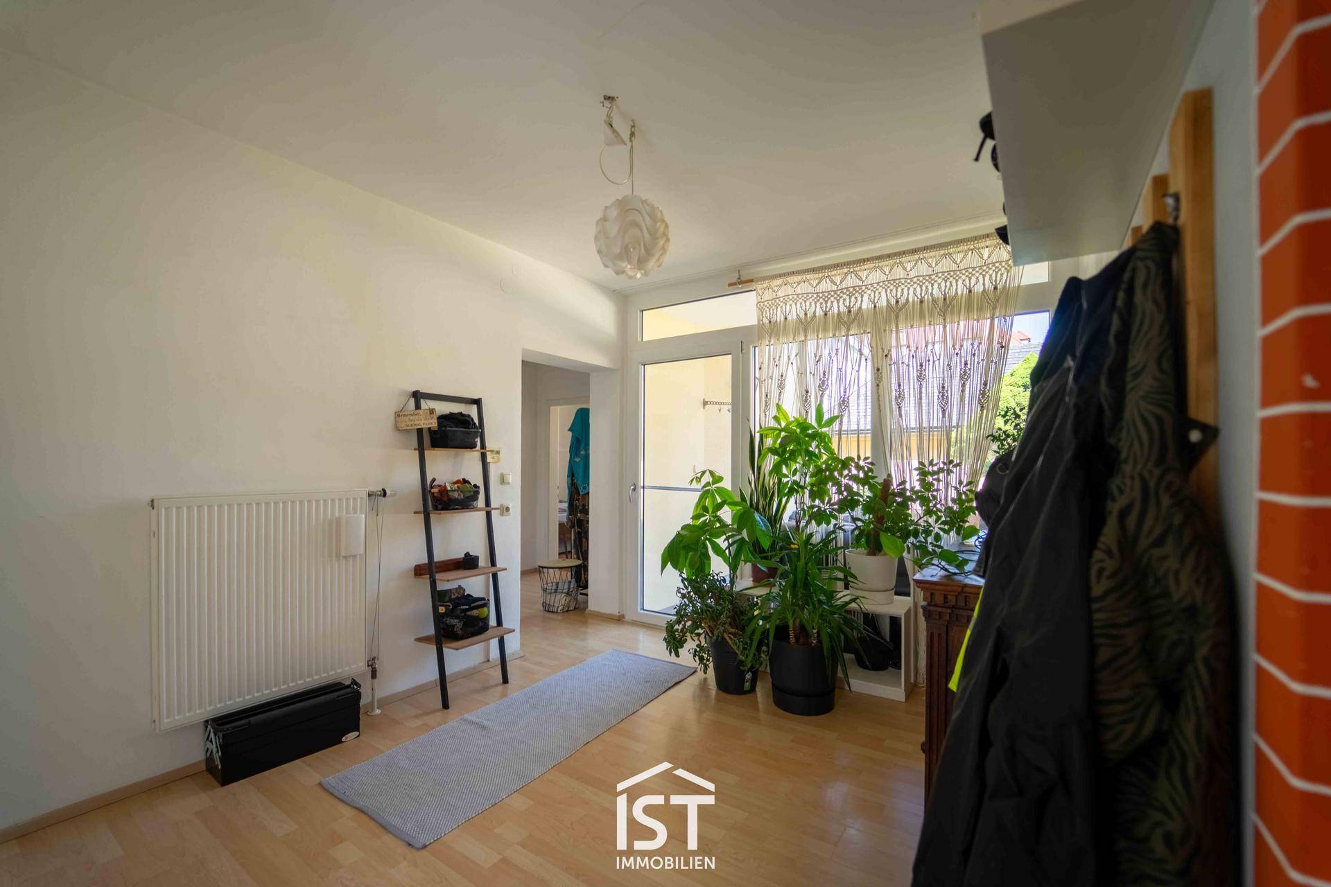 Heller Eingangsbereich mit vielen Pflanzen, Garderobe und Zugang zum Außenbereich.