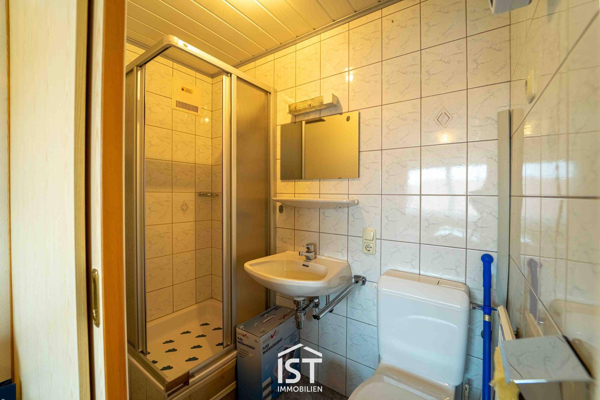 Kleines Badezimmer mit Duschkabine, Waschbecken und WC, komplett gefliest.