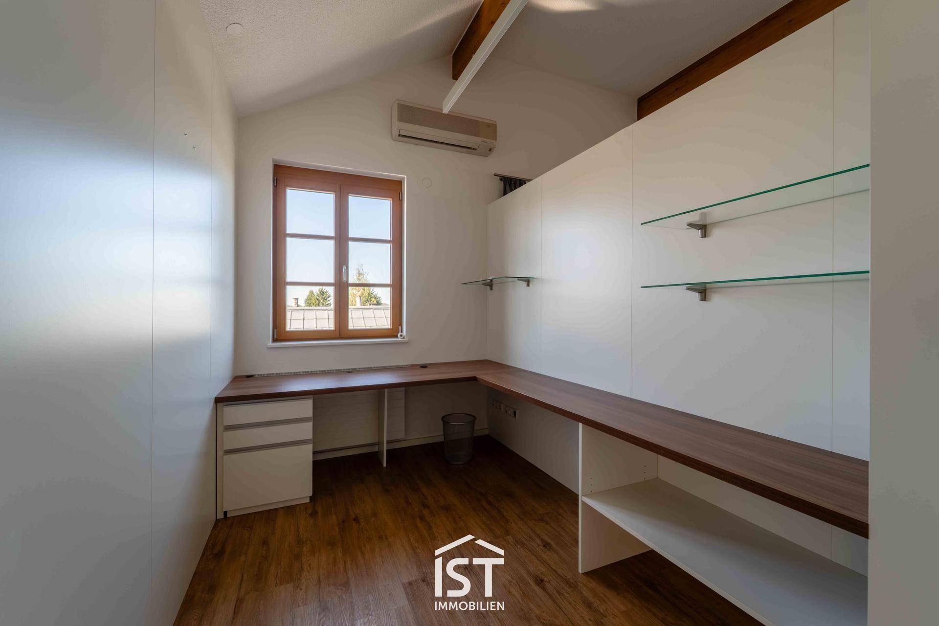 Helles Arbeitszimmer mit großem Schreibtisch, Holzfußboden und Fenster mit Ausblick.