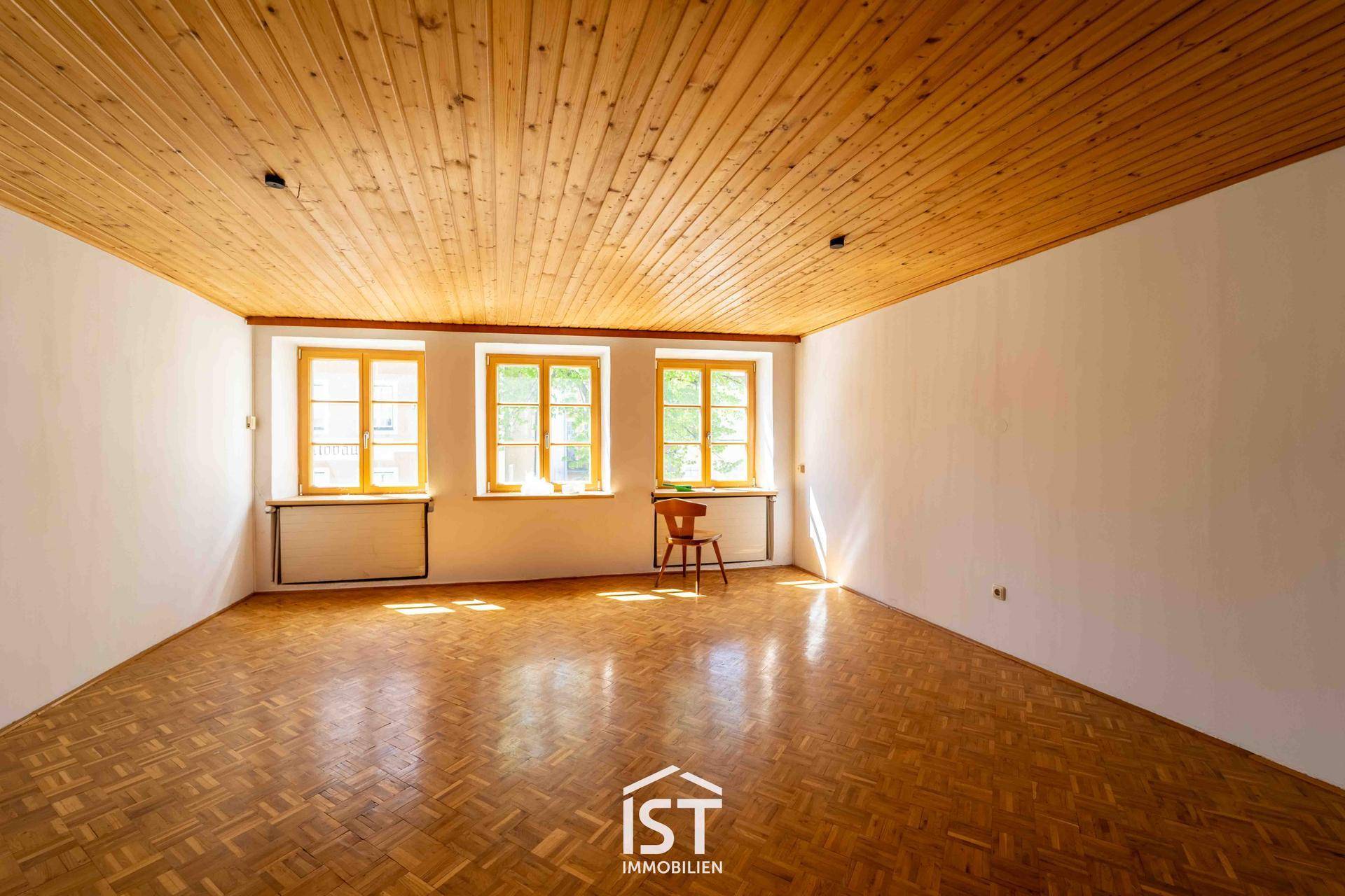 Heller, leerer Raum mit Holzdecke und Parkettboden, durchflutet von Tageslicht.