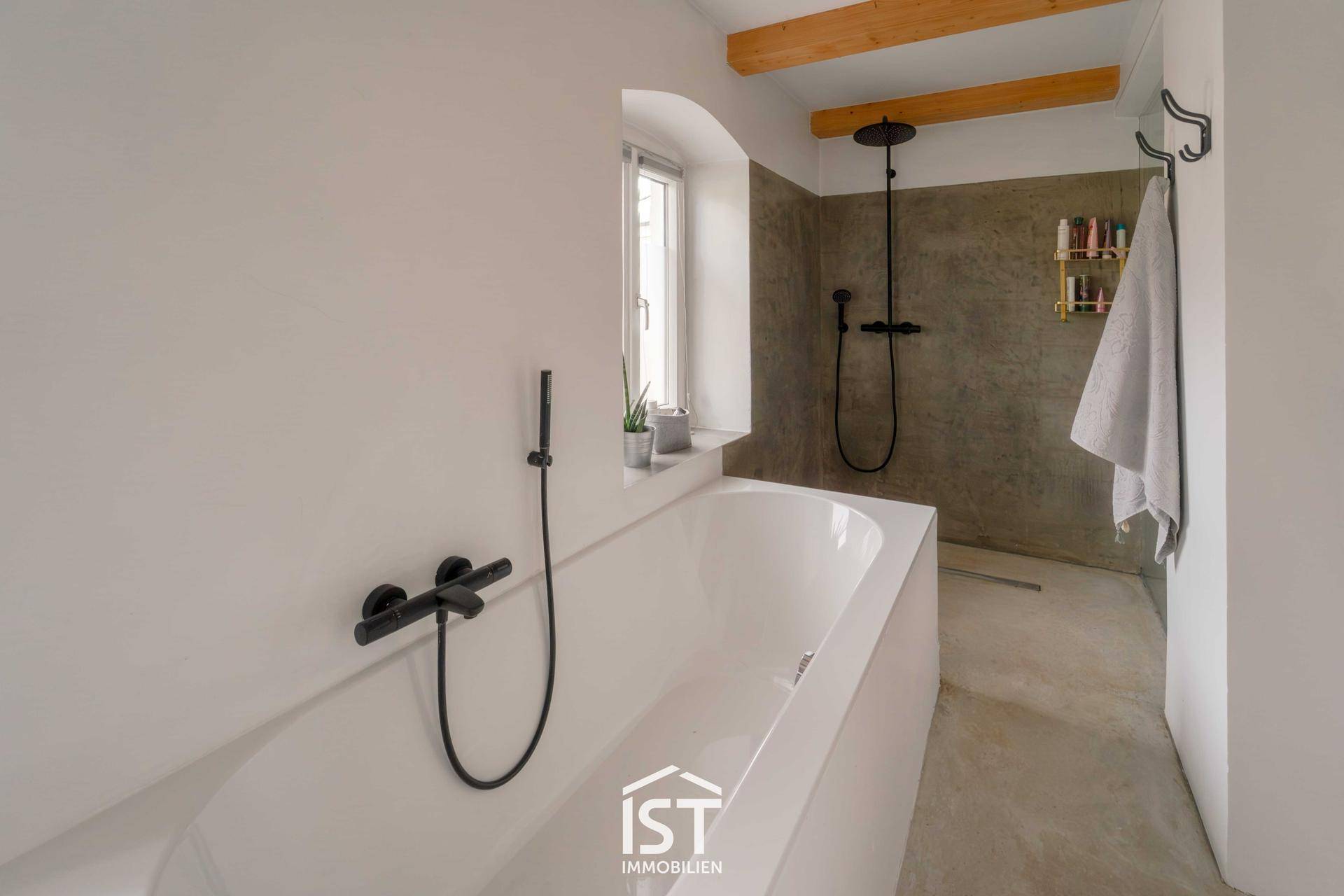 Modernes Badezimmer mit Badewanne, Regendusche und dunklen Armaturen.