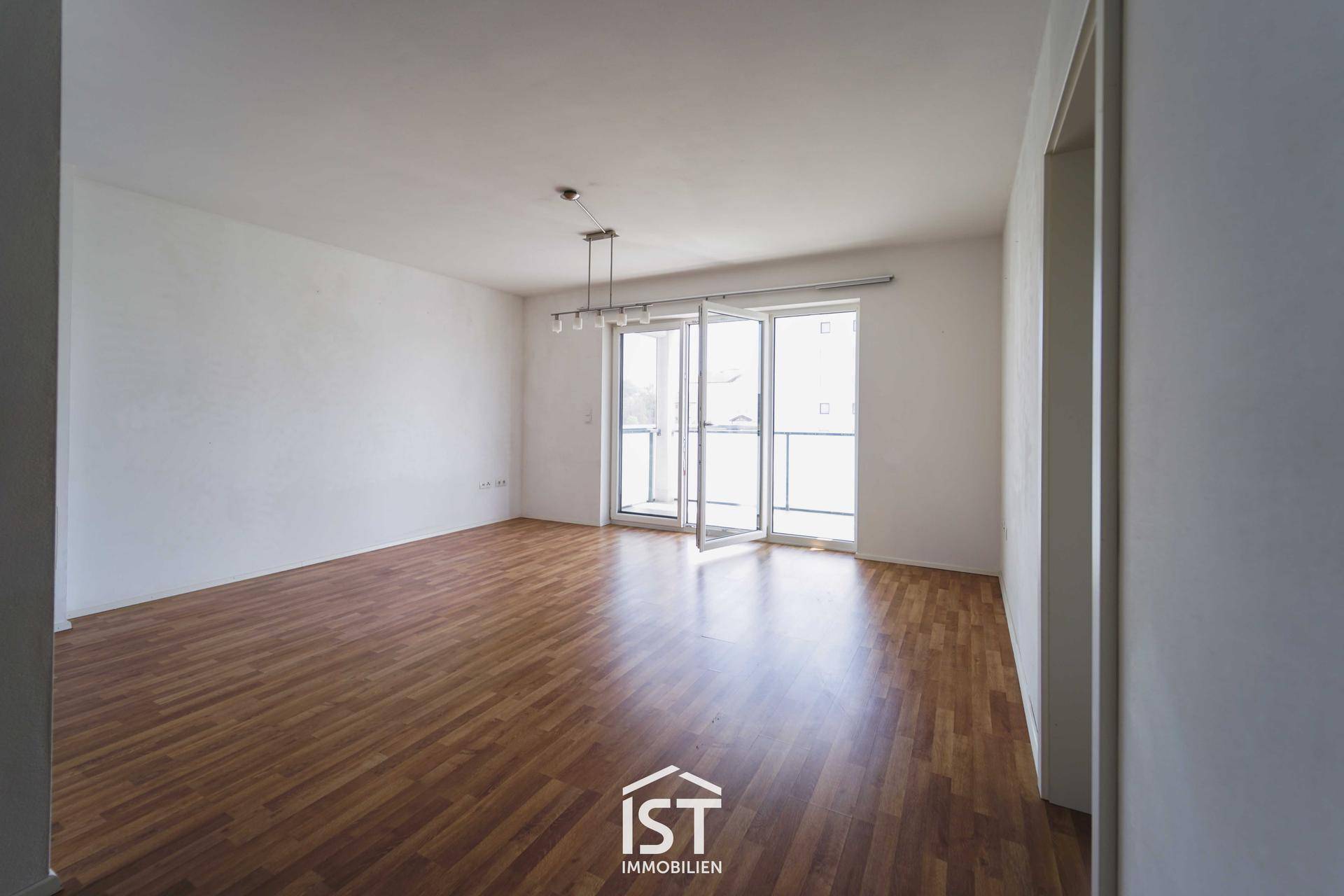 Heller Wohnbereich mit Holzboden und Zugang zu einem Balkon durch große Fenstertüren.