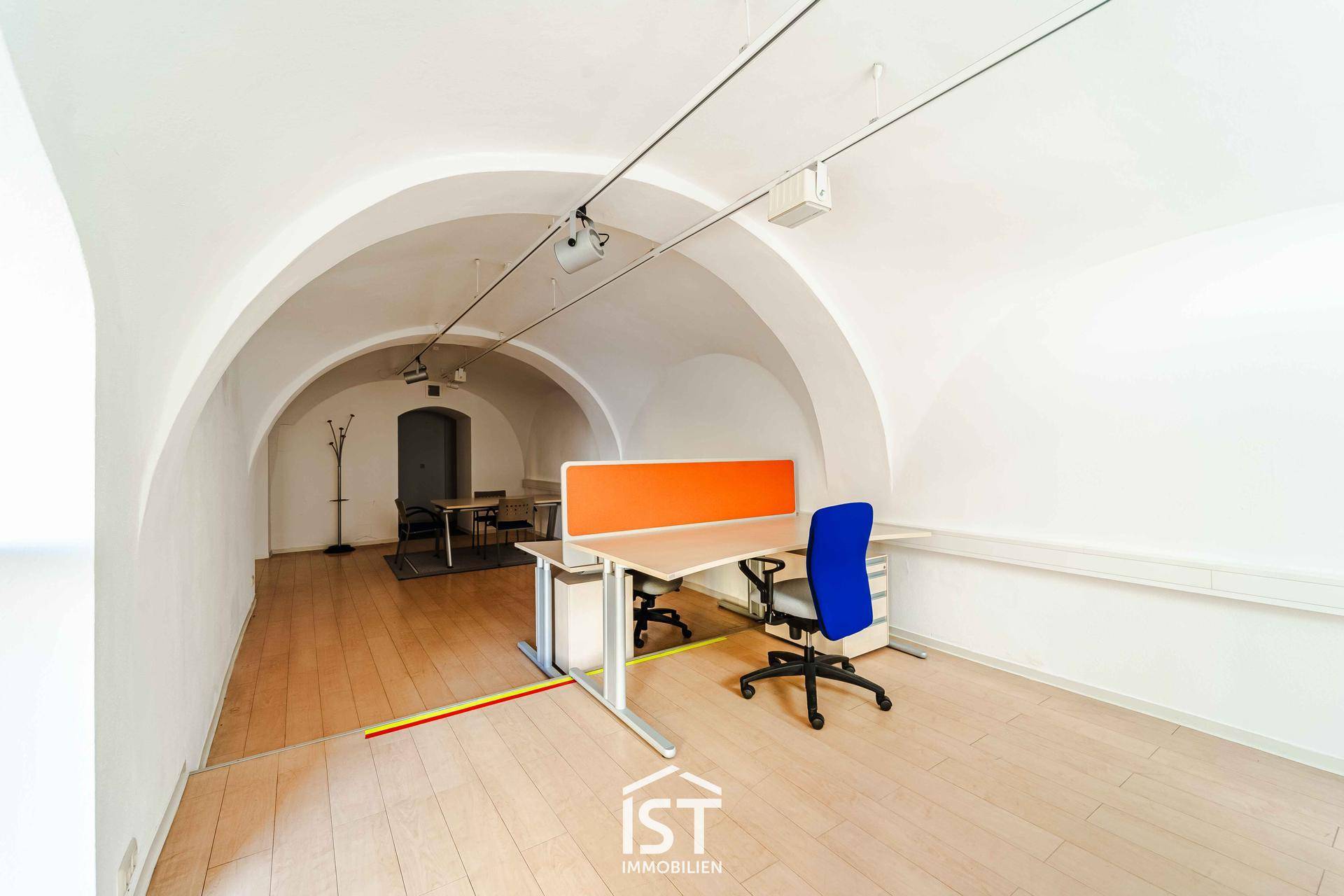 Geräumiger Bürobereich mit beeindruckenden Gewölbedecken, hellem Holzboden und einem modernen Schreibtisch mit Bürostuhl.
