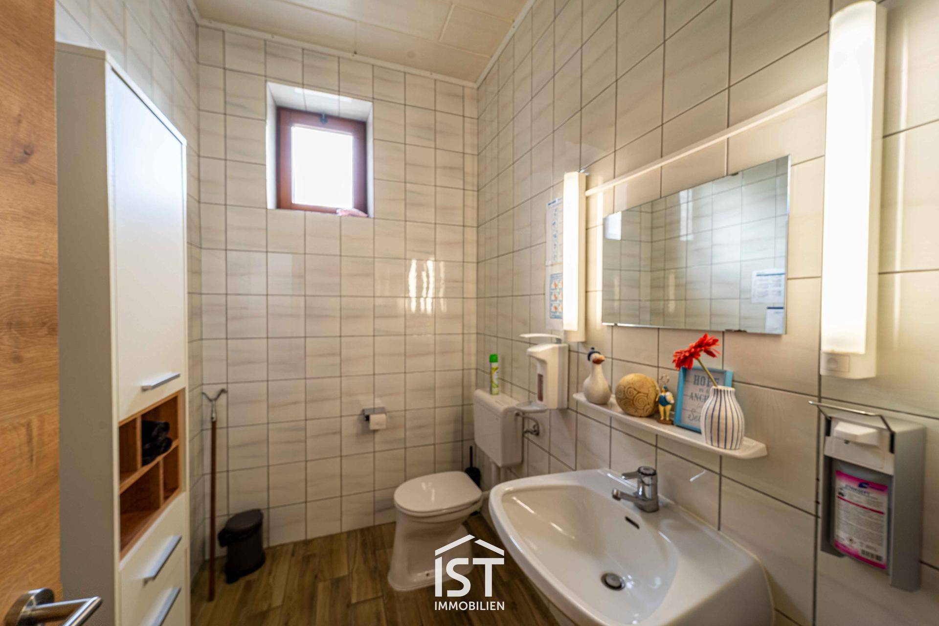Kleines Badezimmer mit Fliesen, Fenster, Waschbecken und Toilette in hellem Design.
