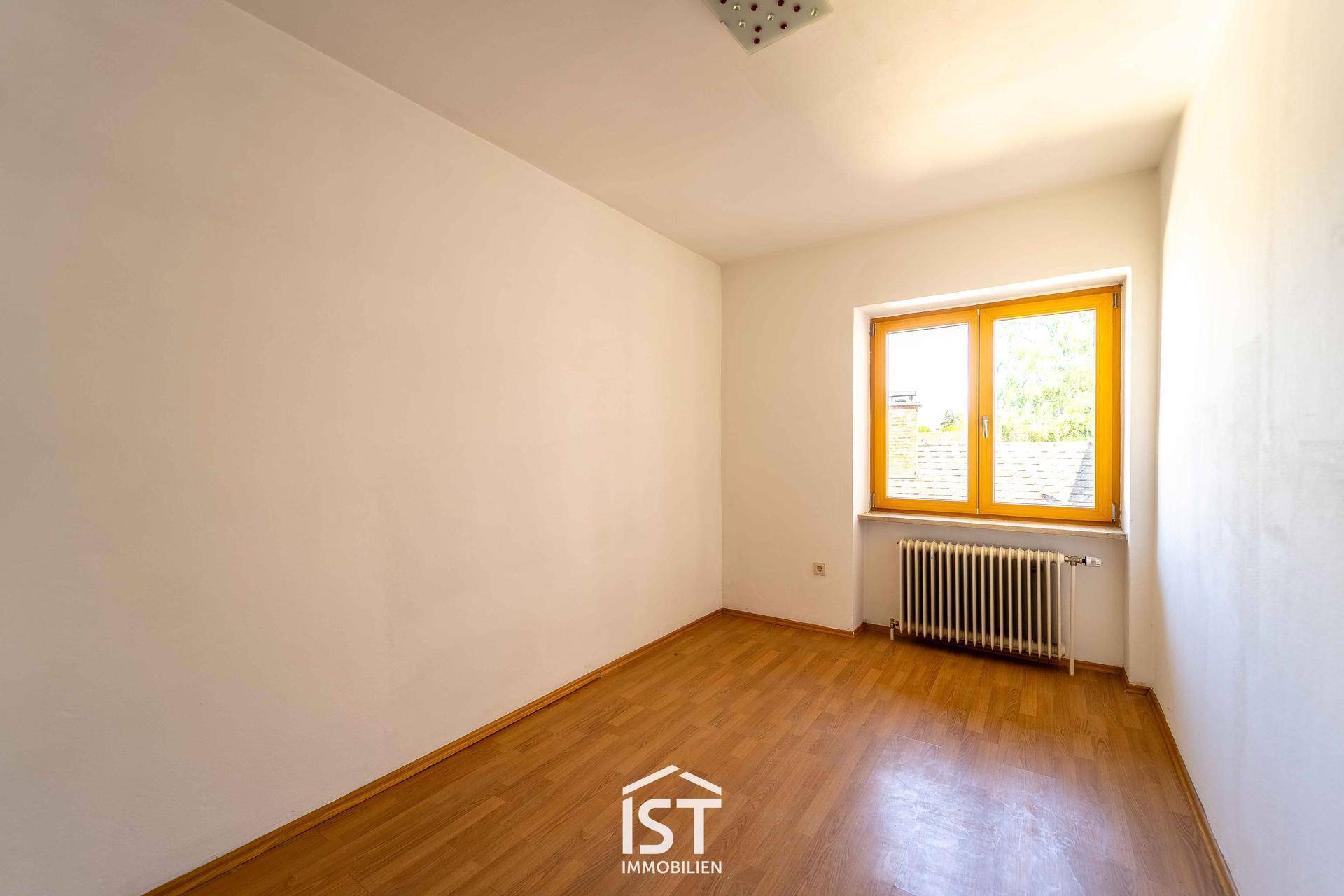 Leerer Raum mit Parkettboden und Fenster, das viel Sonnenlicht hereinlässt.