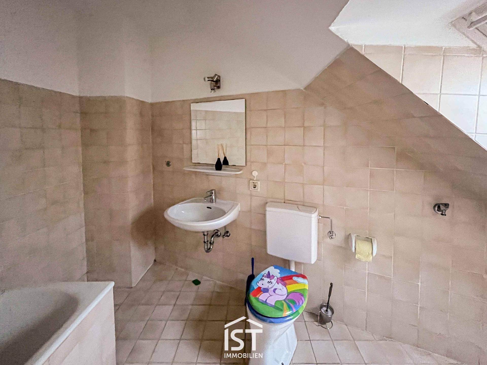 Badezimmer im Dachgeschoss mit Badewanne, Waschbecken und beigen Fliesen an Wänden und Boden.
