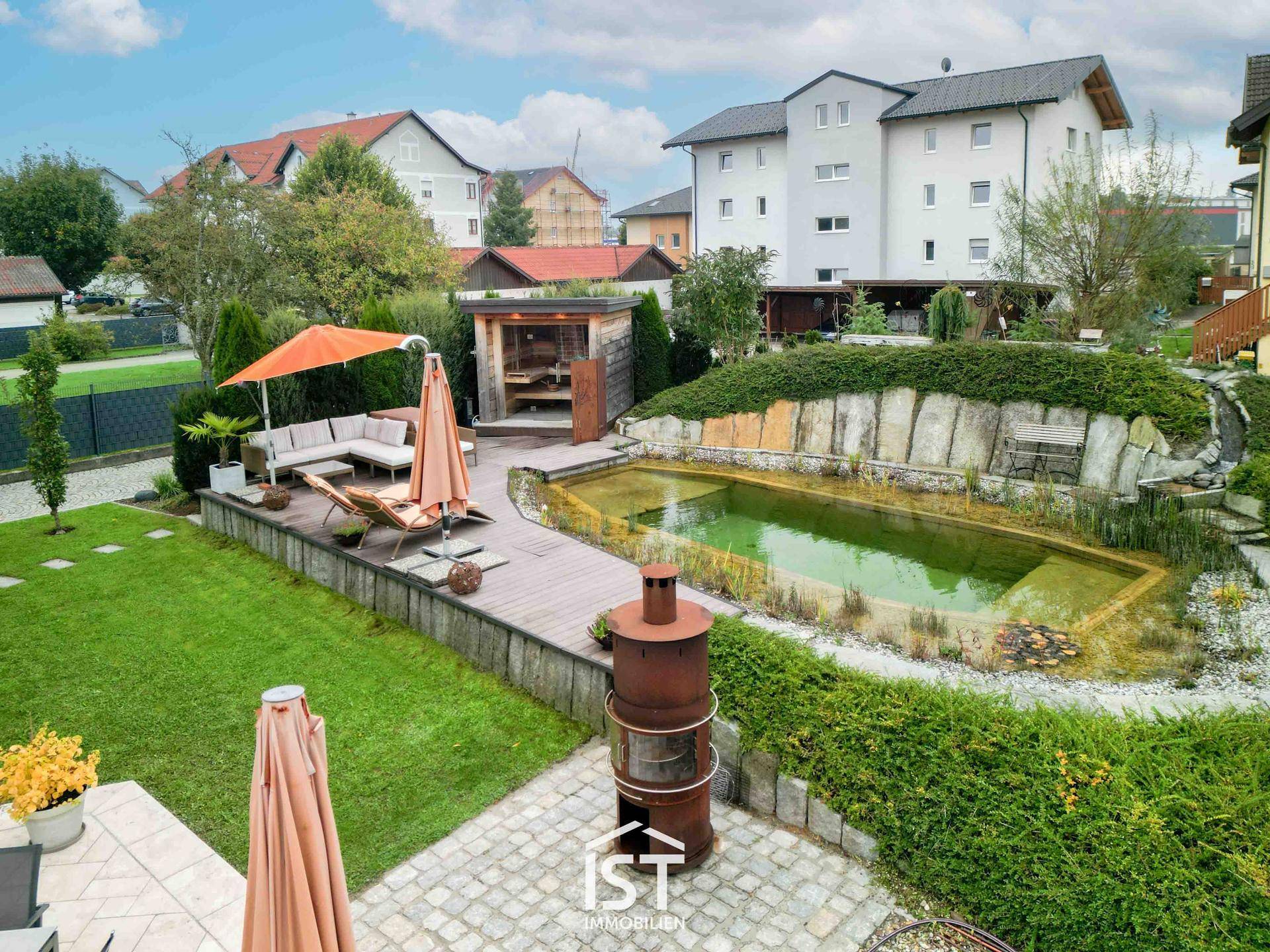 Vogelperspektive des Gartens mit Naturpool, Holzdeck und Grillbereich.