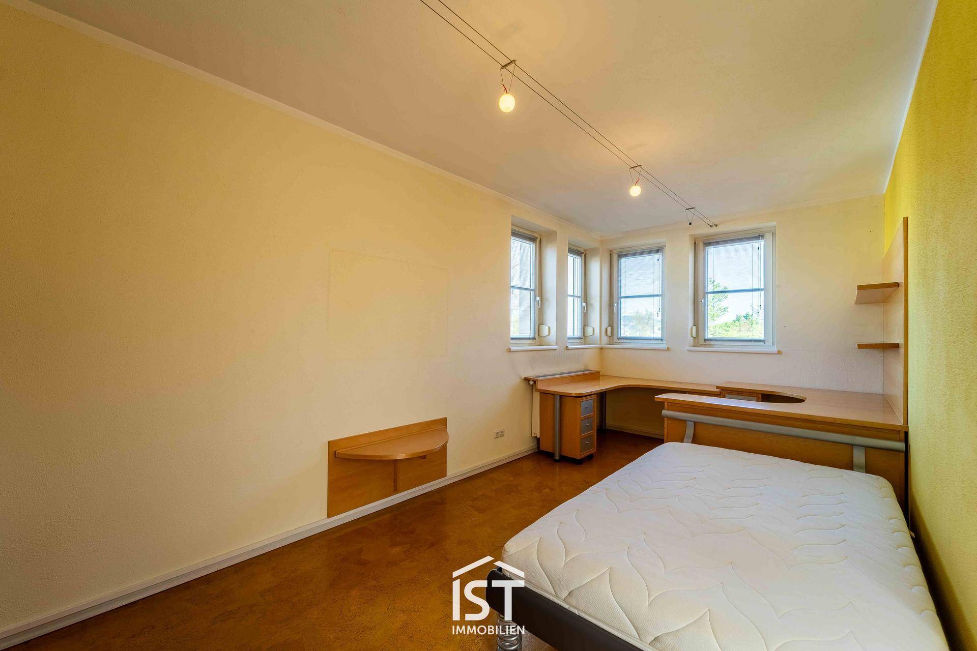 Schlafzimmer mit Schreibtisch, Bett und mehreren Fenstern für viel Tageslicht.