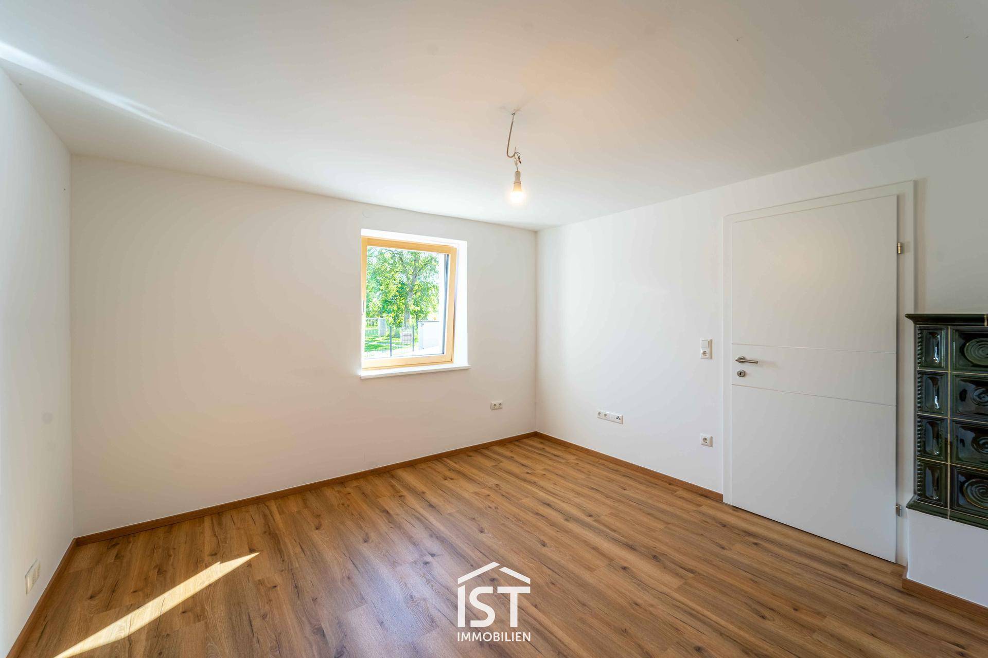 Helles Zimmer mit Laminatboden und einem dekorativen Kachelofen, bereit zur individuellen Gestaltung.