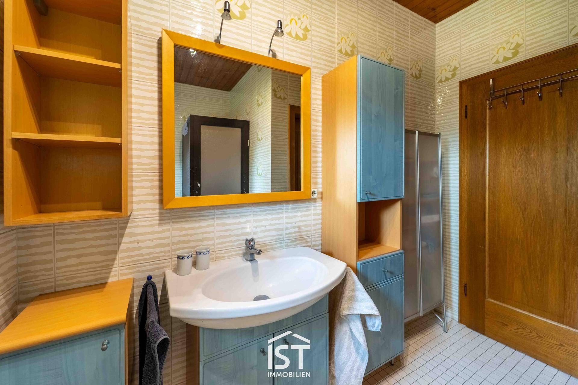 Badezimmer mit Einzelwaschbecken, Spiegelschrank und hellen Fliesen an Wänden und Boden.