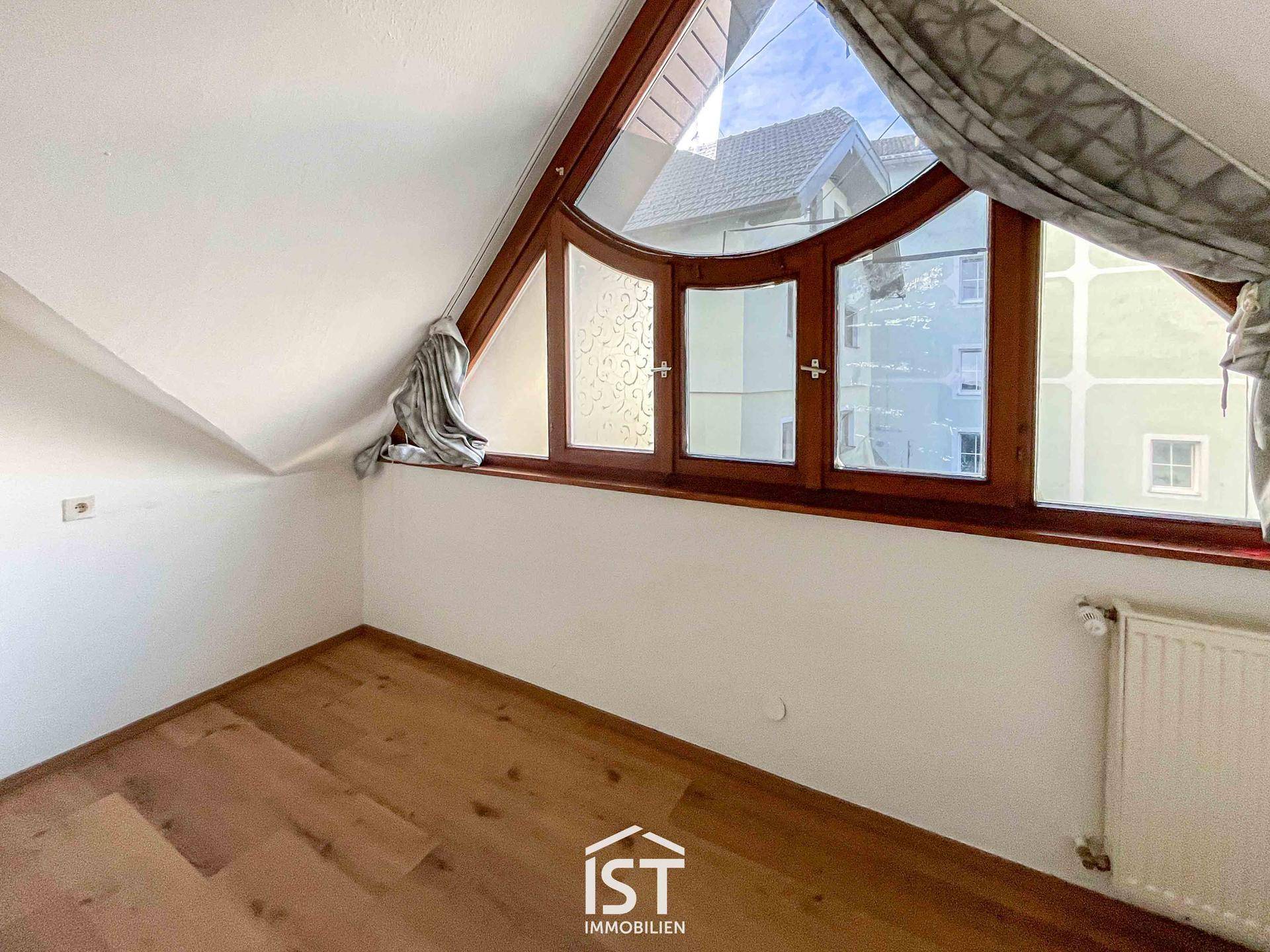 Dachzimmer mit einzigartigem Bogenfenster und Holzboden, das viel Licht hereinlässt.