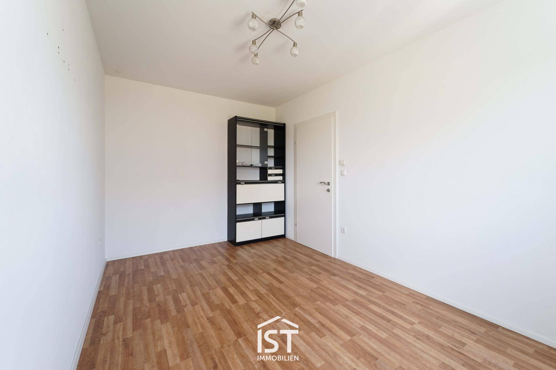 Helles Zimmer mit Holzboden, weißen Wänden und einem modernen Schrank.