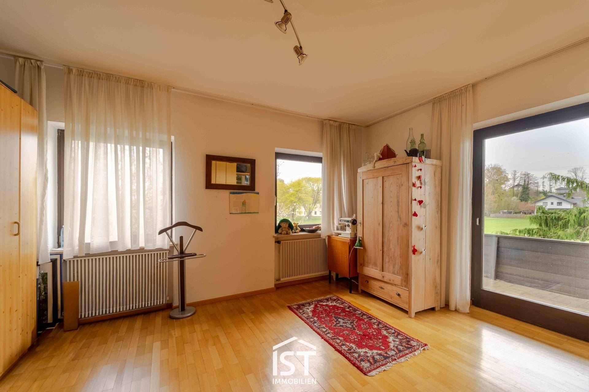 Helles Schlafzimmer mit Parkettboden, Kleiderschrank und Zugang zu einem Balkon.