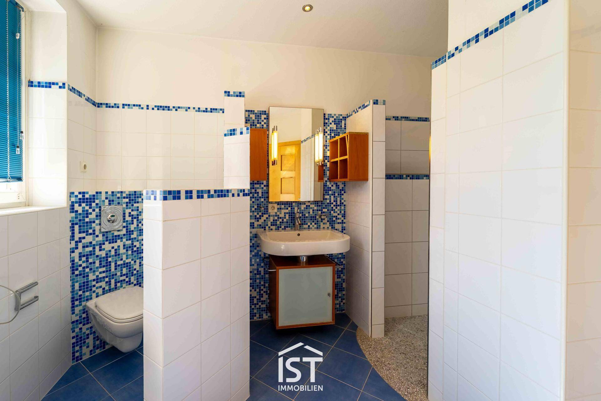 Modernes Badezimmer mit blauen Mosaikfliesen, Dusche und wandhängendem WC.