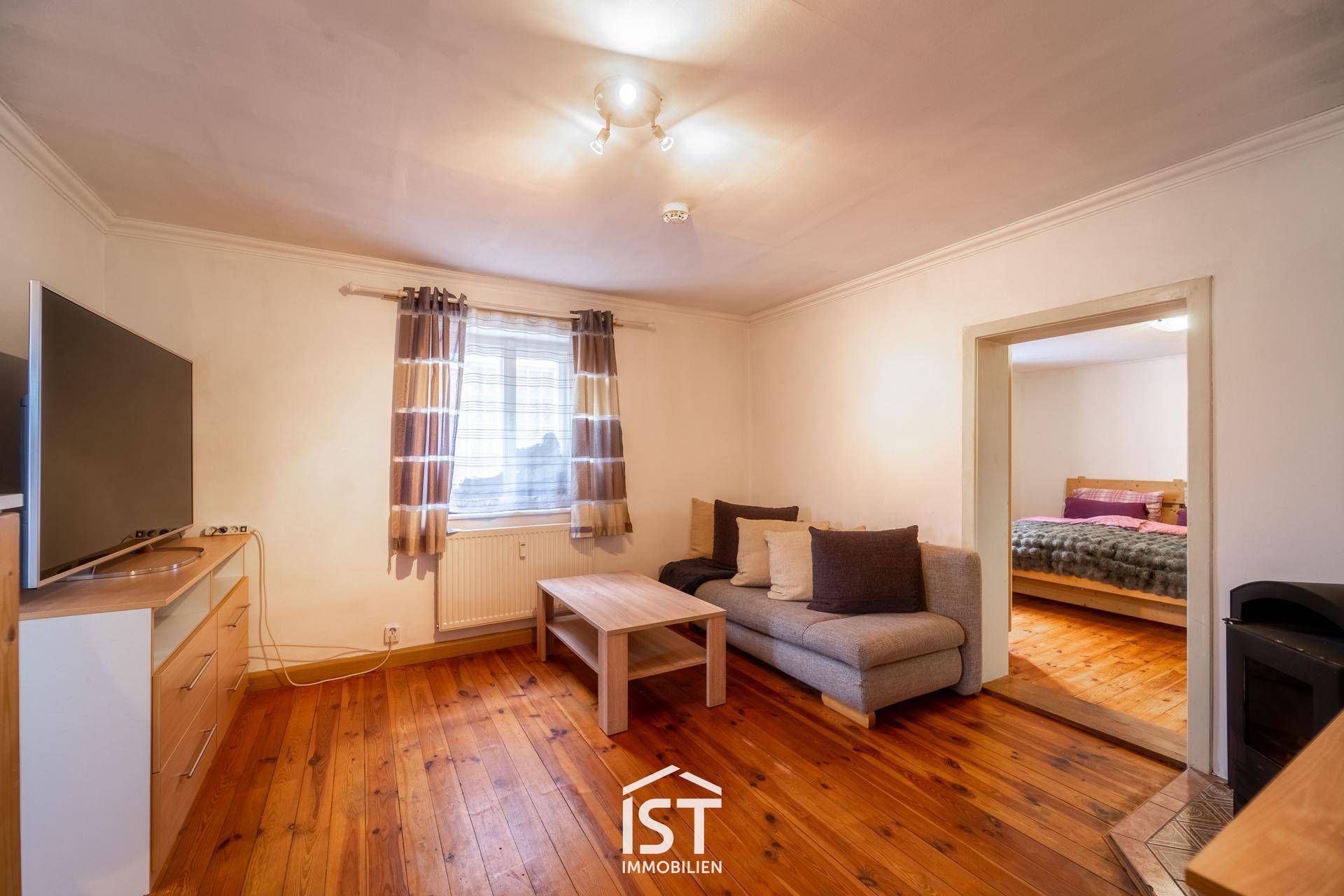 Wohnzimmer mit Holzboden, bequemer Couch und Blick in ein angrenzendes Schlafzimmer.