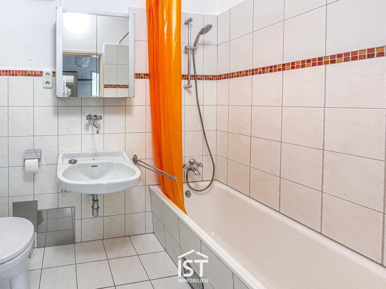 Badezimmer mit Badewanne, Duschvorhang und weißen Fliesen mit dekorativer Bordüre.