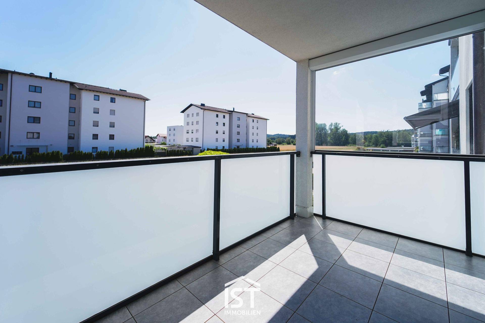 Geräumiger Balkon mit Fliesenboden, Milchglasbrüstung und Blick auf die Umgebung.
