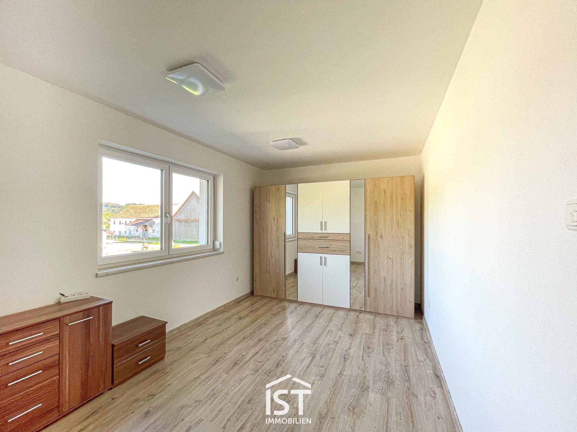 Geräumiges Schlafzimmer mit Laminatboden, großem Fenster und Kleiderschrank.