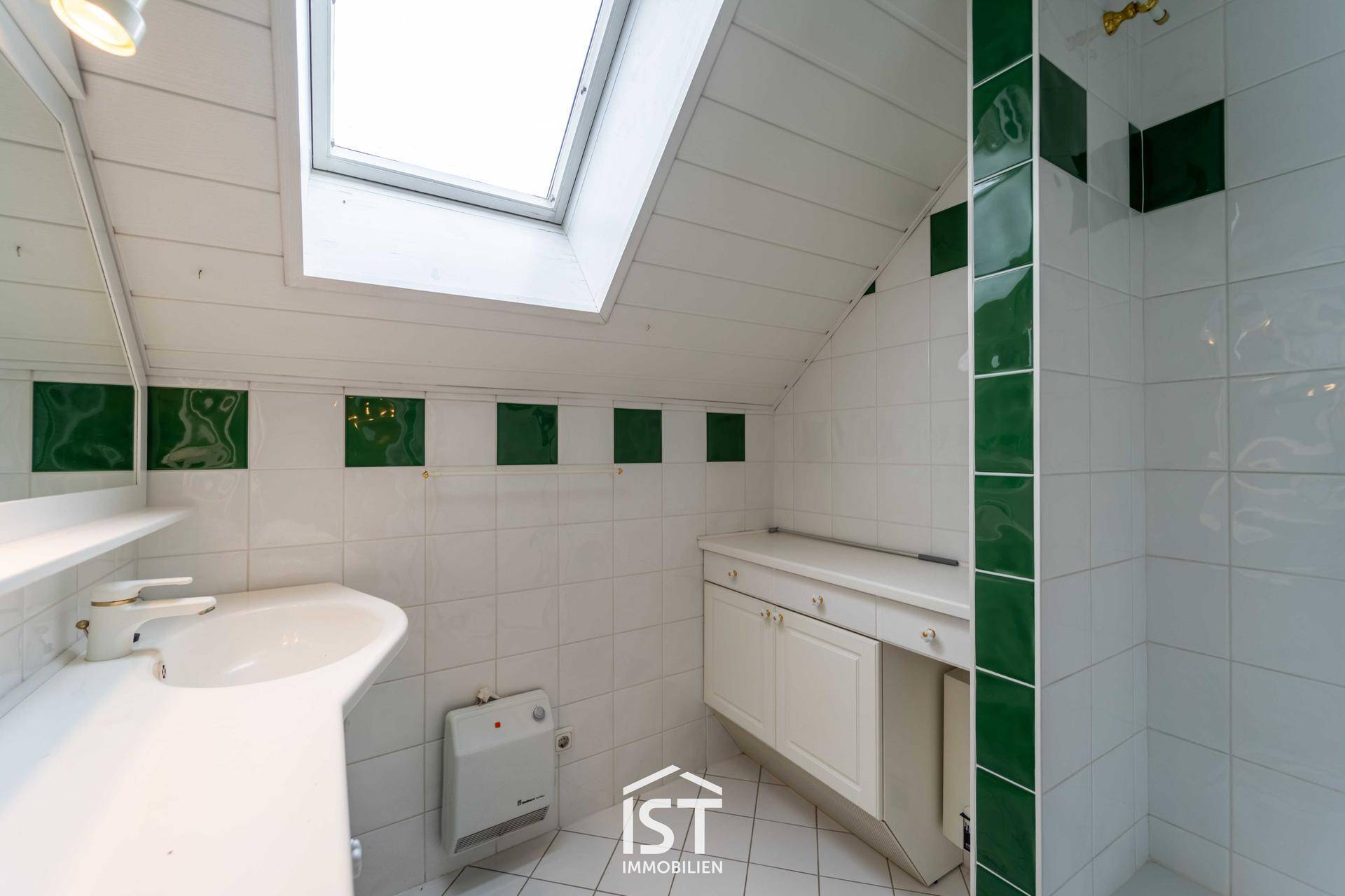 Dachgeschoss-Badezimmer mit Dachfenster, weißen und grünen Fliesen und Dusche.