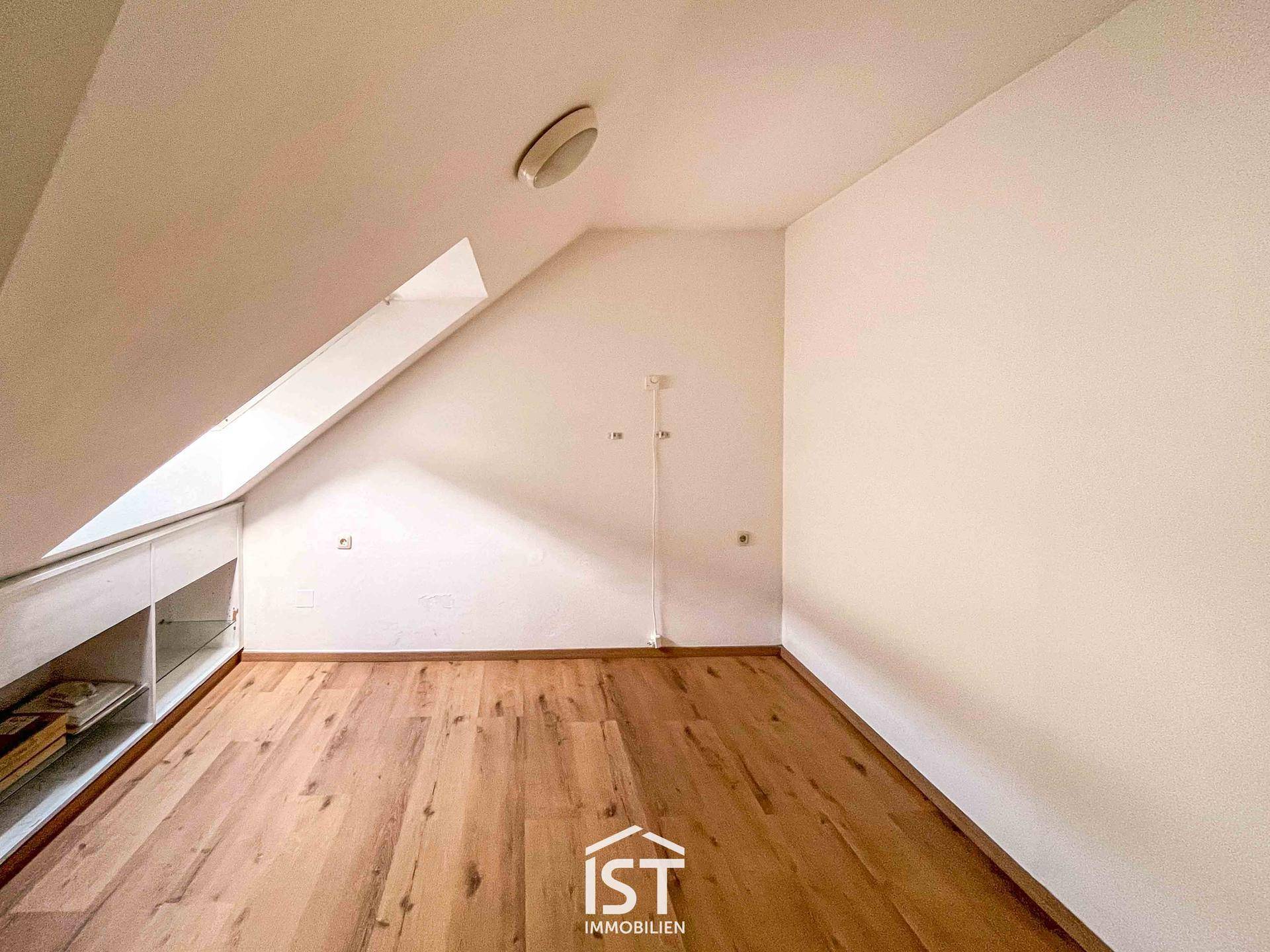 Helles Dachzimmer mit Holzboden und praktischen Einbauschränken unter der Dachschräge.