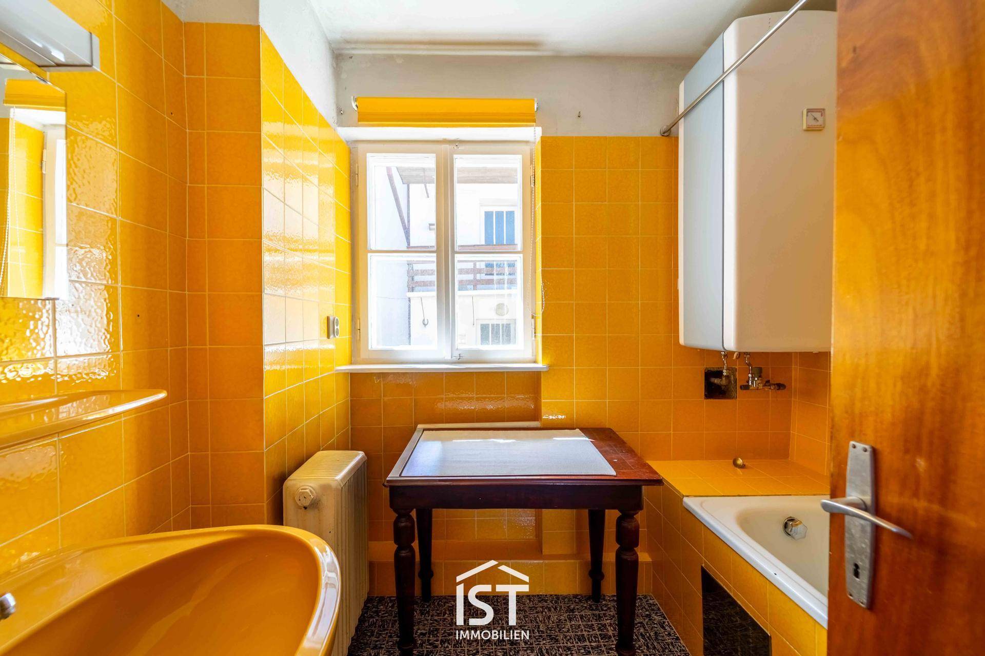 Badezimmer mit auffälligen gelben Fliesen, Badewanne und Fenster.