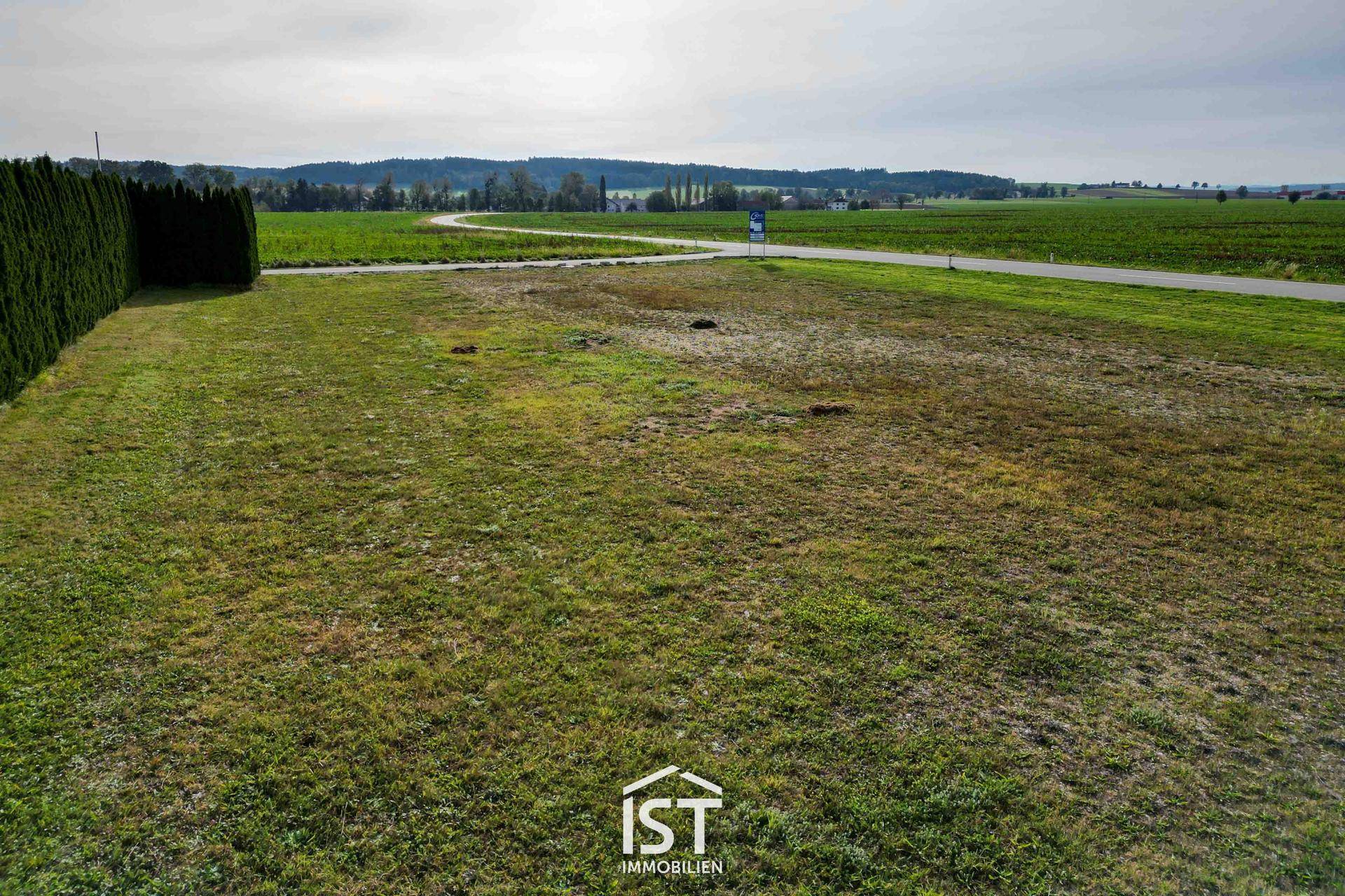 Blick über das grüne Grundstück in die weite Landschaft mit Feldern und bewaldeten Hügeln am Horizont.